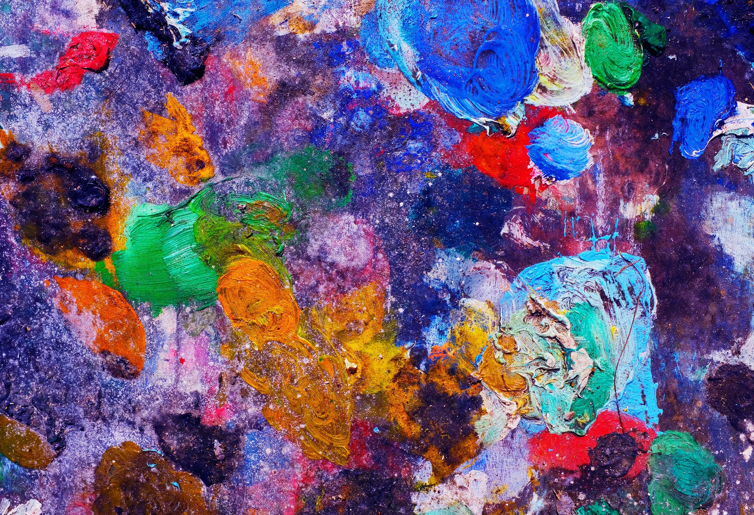 Close-up of an abstract painting with vibrant colors including blue, green, orange, red, purple, and hints of yellow, created with thick textured brushstrokes and splattered paint.