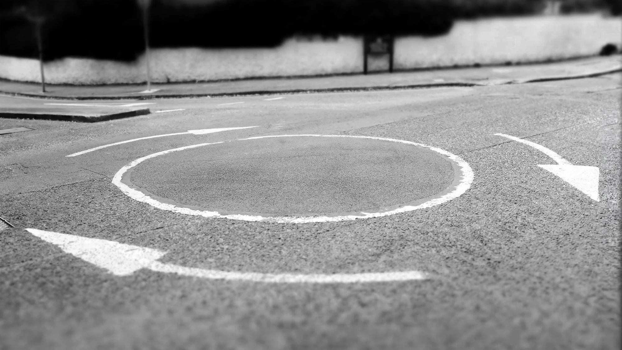 A black and white photo of a parking lot with a painted circular spot and an arrow indicating direction.