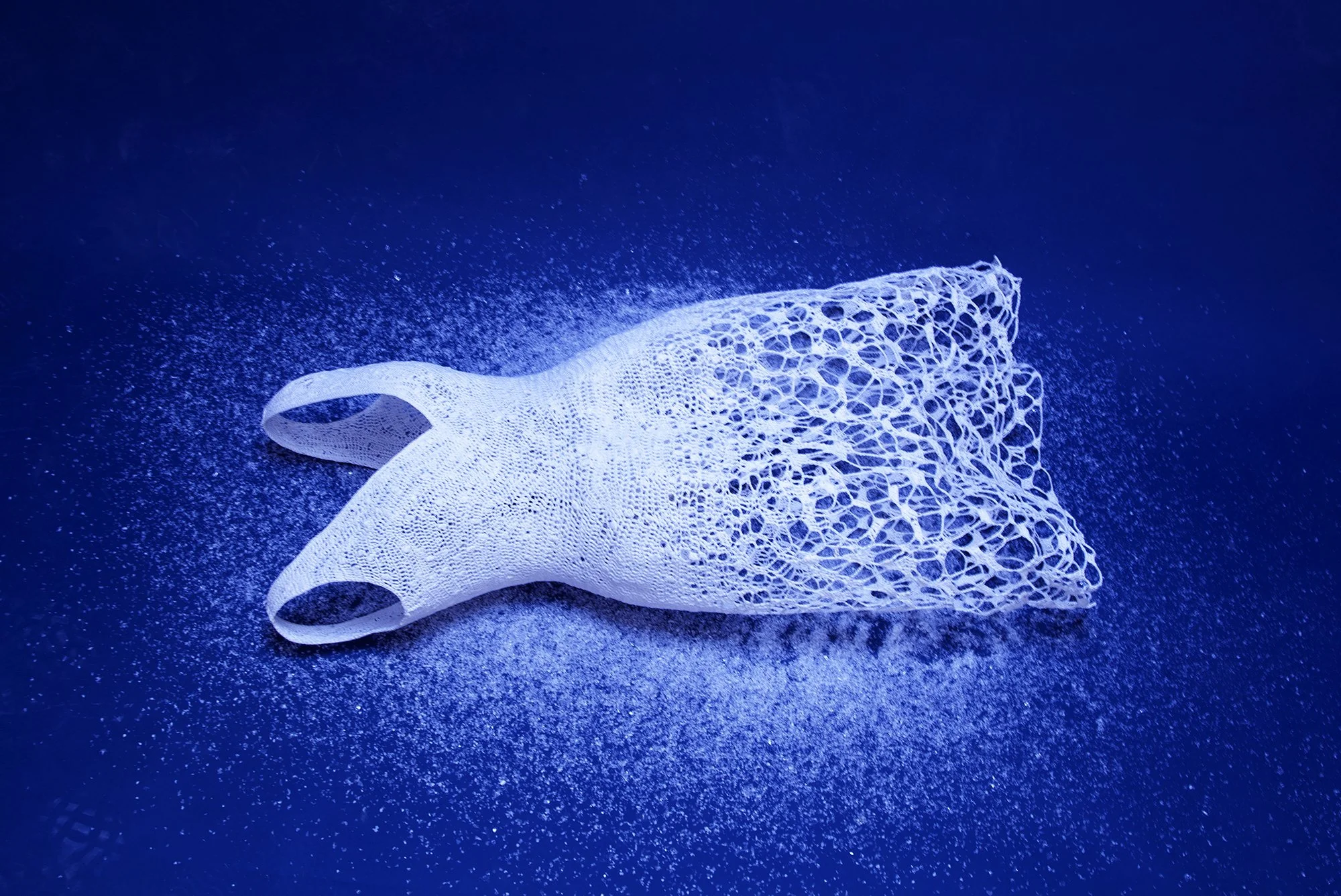 A white, intricately designed 3D-printed structure resembling a skeletal or organic form on a dark blue background with speckled patterns.