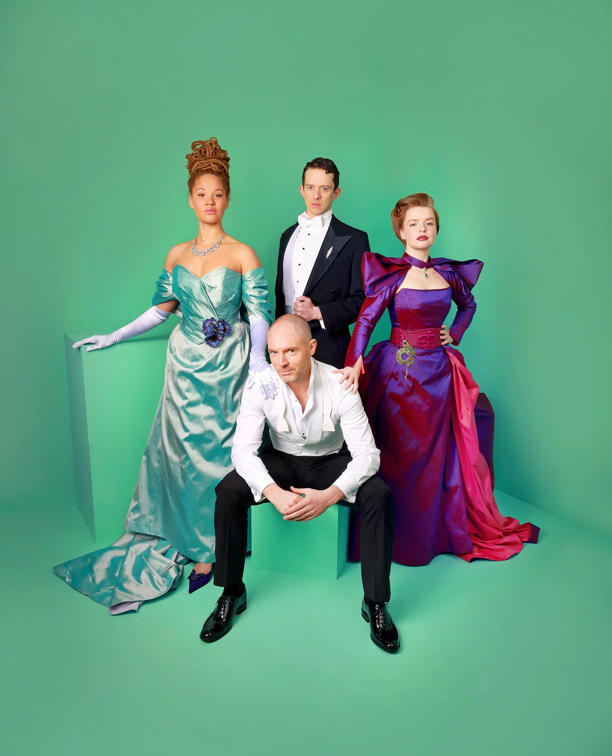 Four people dressed in formal costumes with elaborate dresses and tuxedos, posing against a green background.