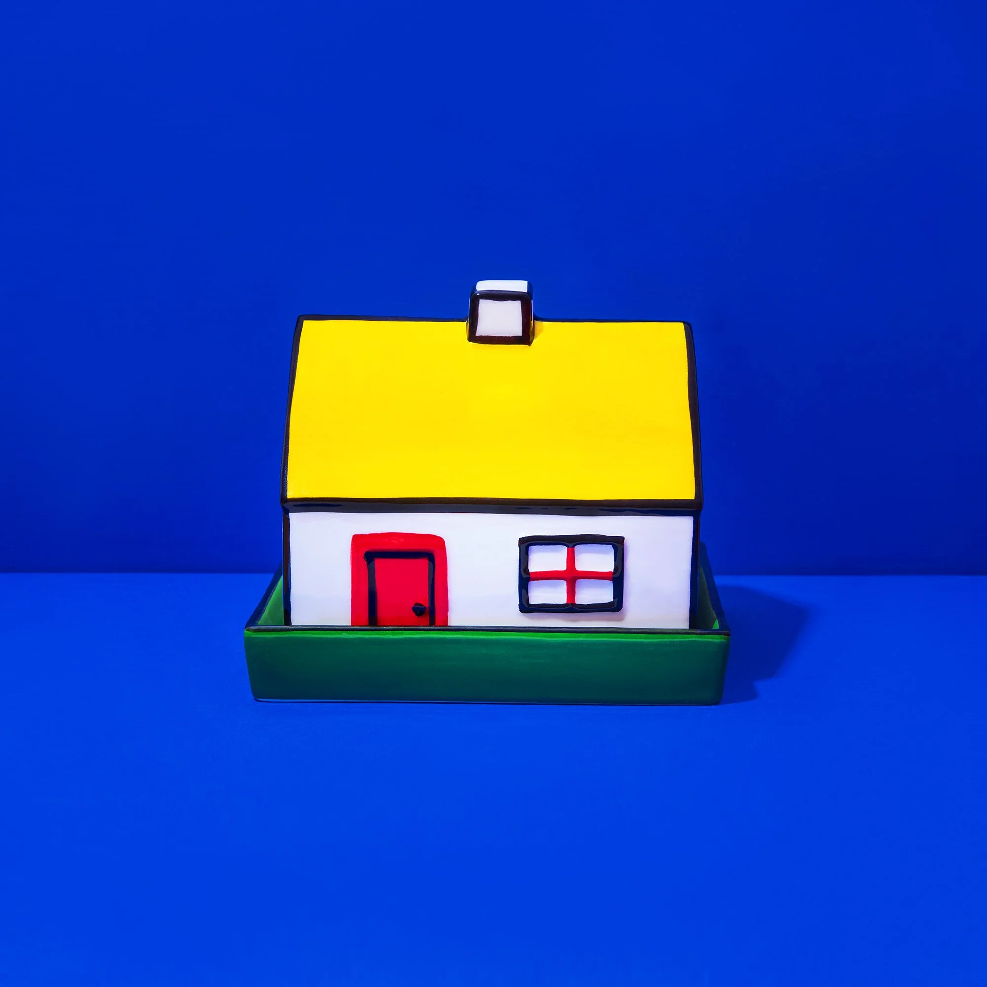 Colorful small house model with a yellow roof, white walls, red door, and windows, set against a solid blue background.