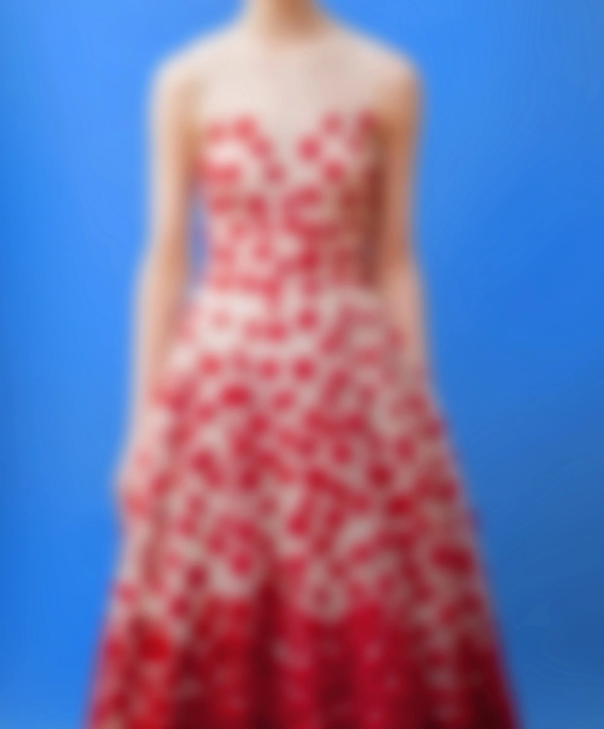 A person with a bare torso wearing a red and white patterned skirt or dress, standing against a blue background.