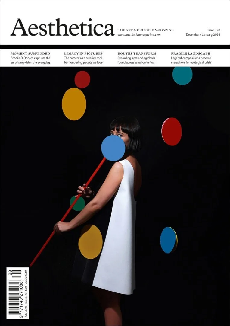 Cover of Aesthetica magazine, issue 128 from December/January 2026, featuring a woman with dark hair and bangs holding a large red stick and blue circle, surrounded by colorful circles against a black background.