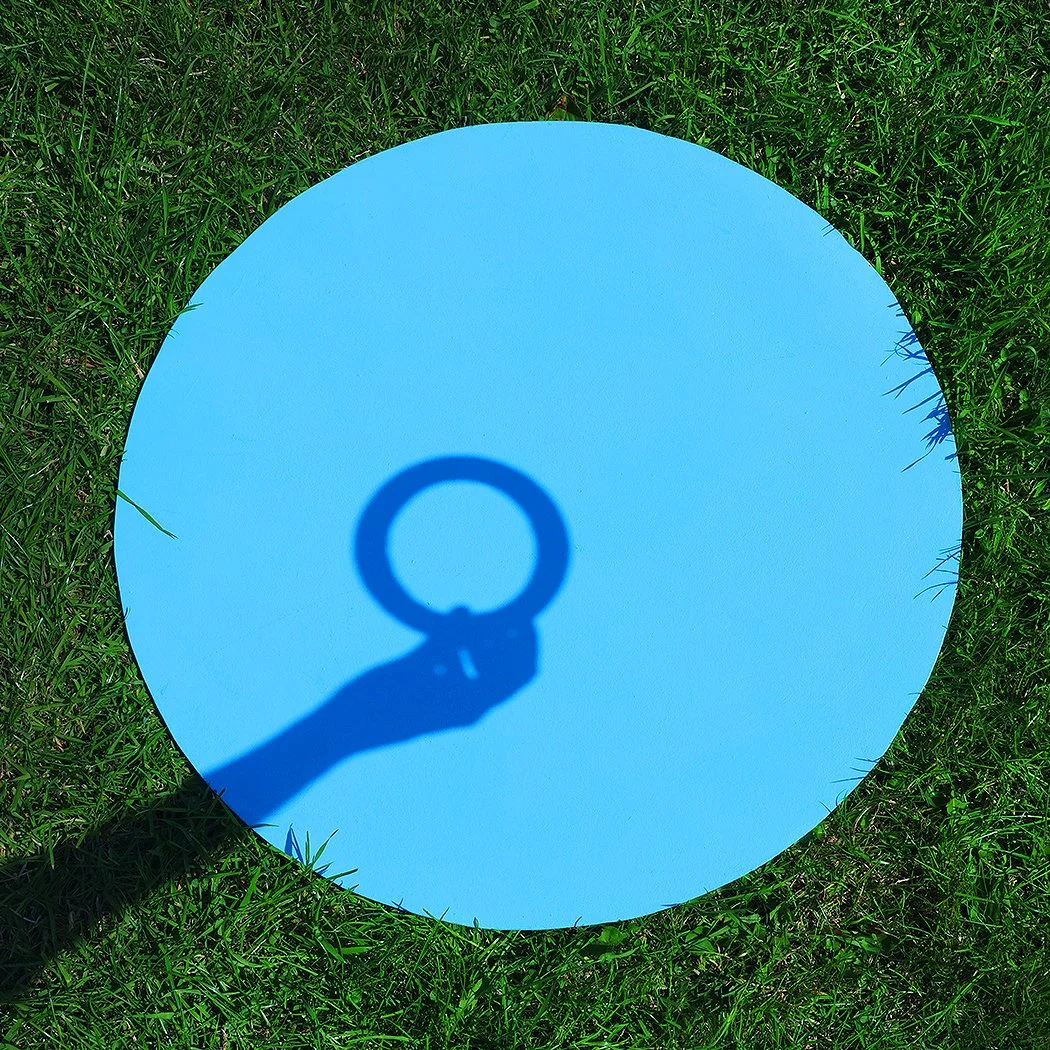 Shadow of a person holding a ring, cast onto a blue circular surface on grass