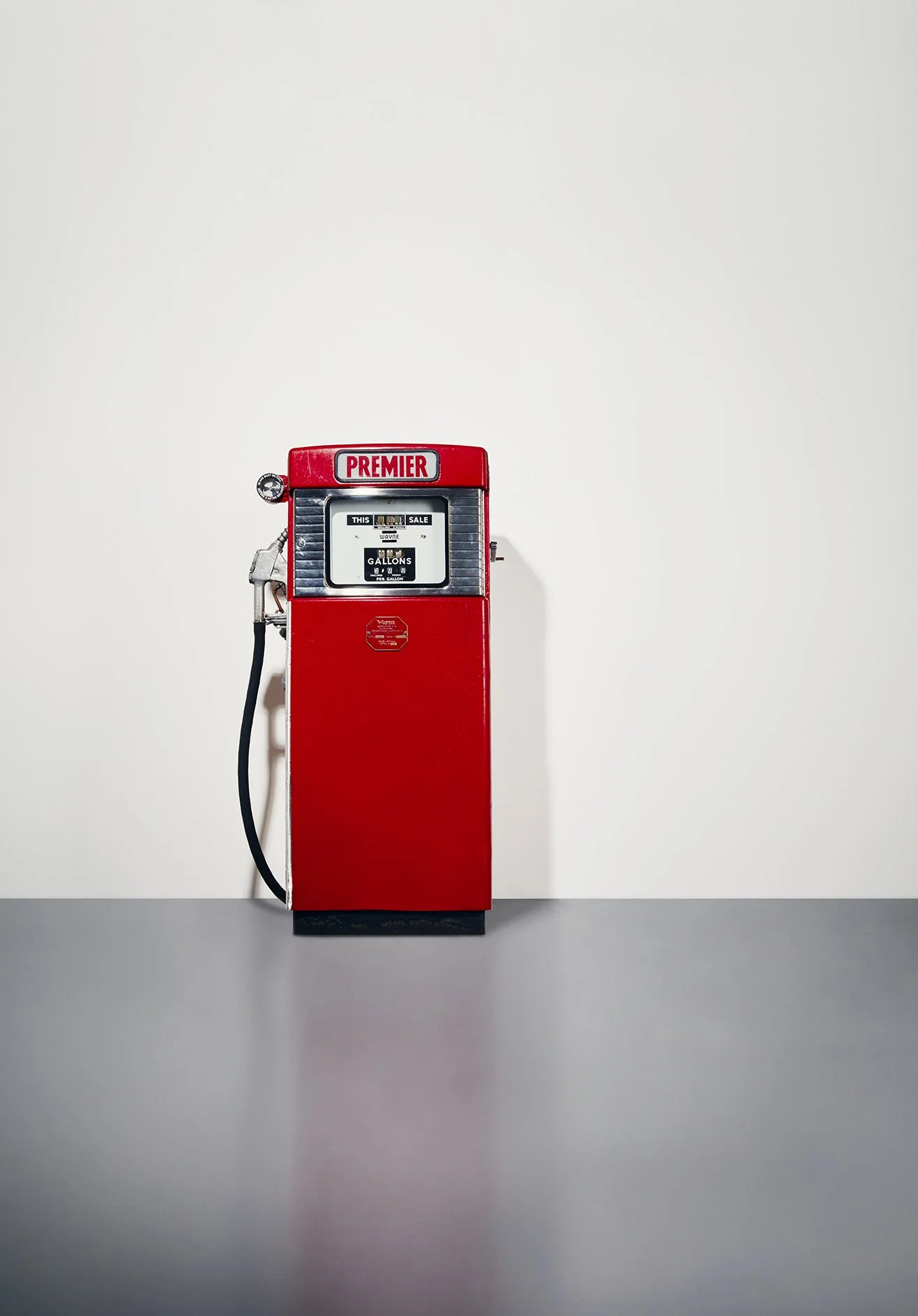 Red vintage gas pump against plain white wall with gray surface.