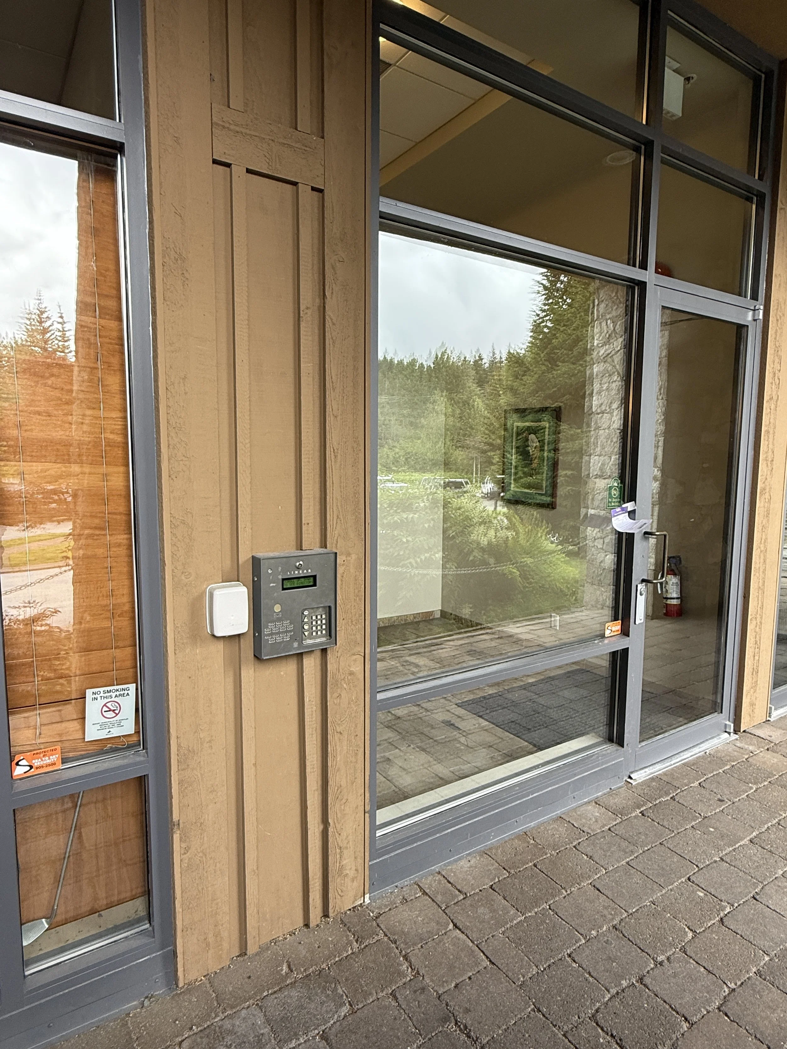 Glass door entrance with wooden siding, security keypad, no smoking sign, and fire extinguisher inside.
