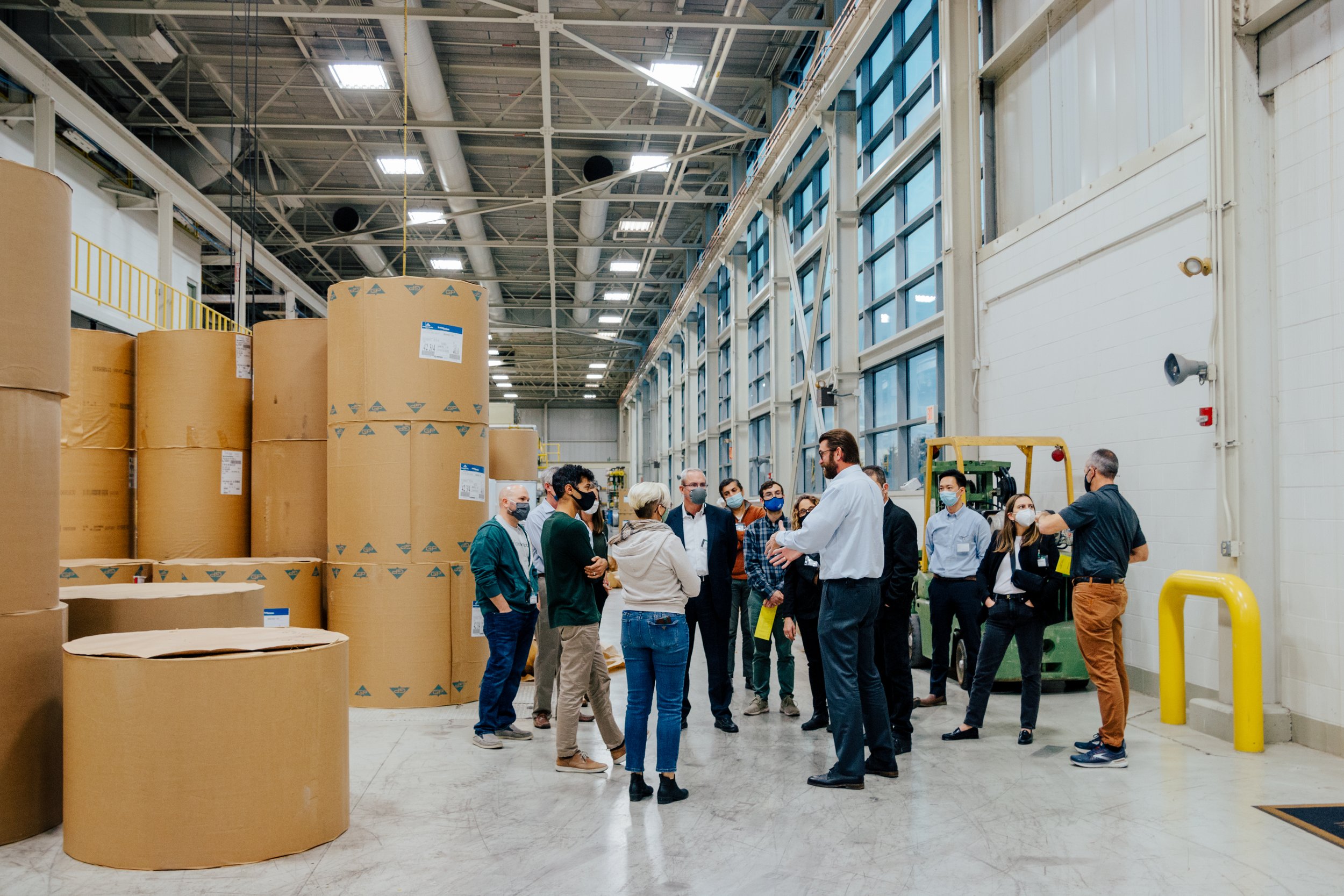 A groups of people gathered in a warehouse taking a tour.