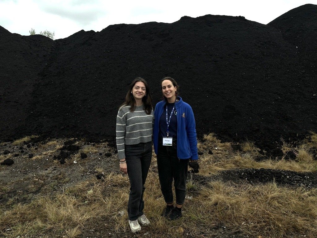 Photo of RRSers Anna and Katelyn in front of a large compost pile