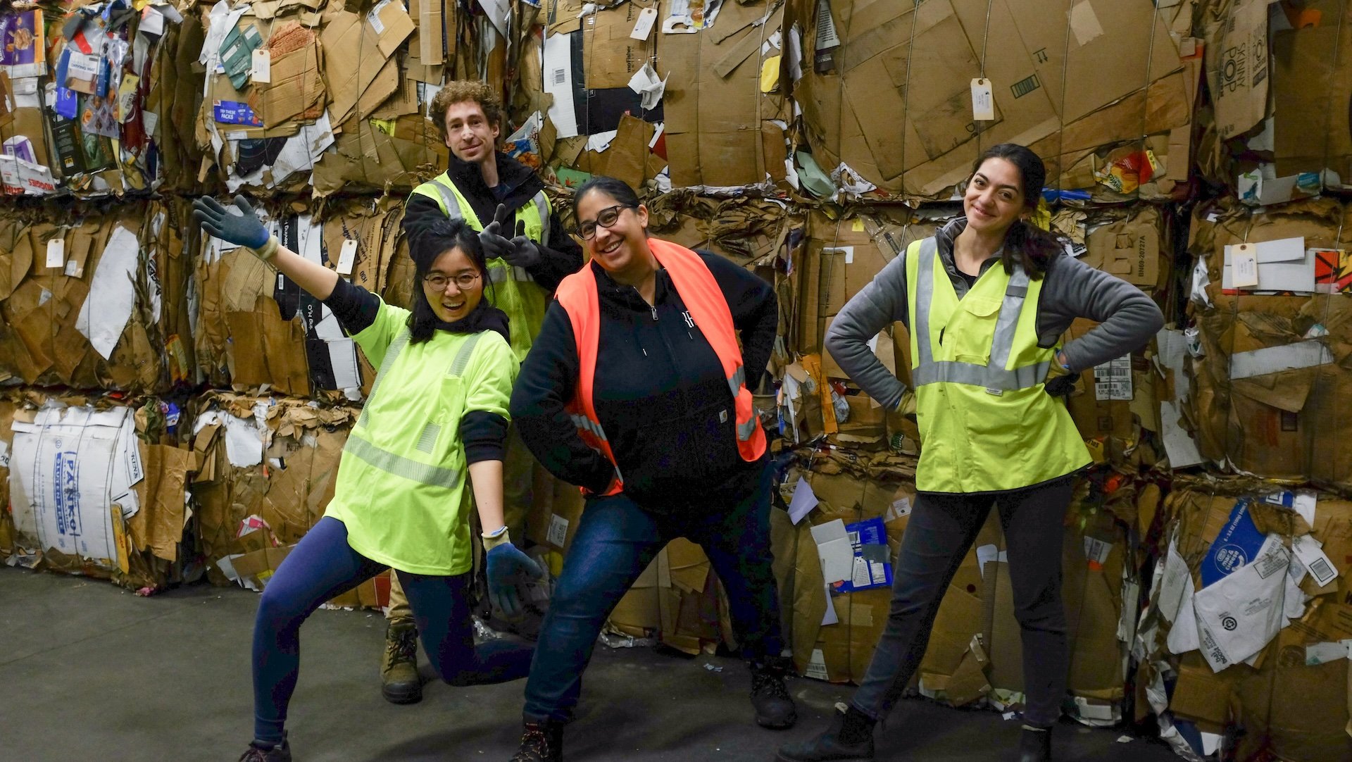 Four people smiling in front of bales of recycled paper