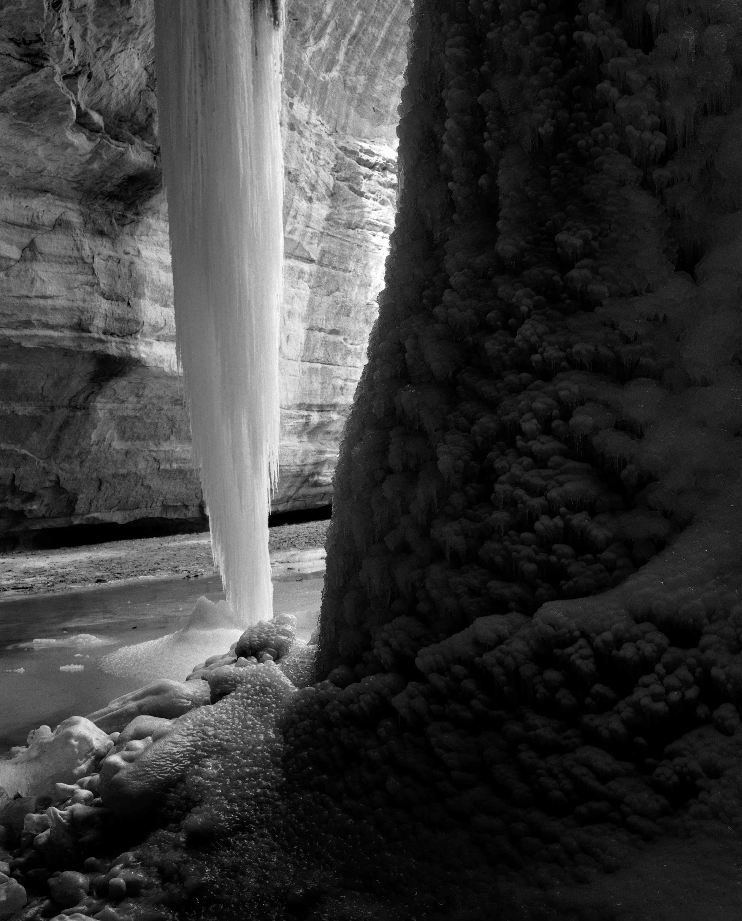 Frozen waterfall flowing down a rock formation with ice and snow around, in a cavern or canyon.