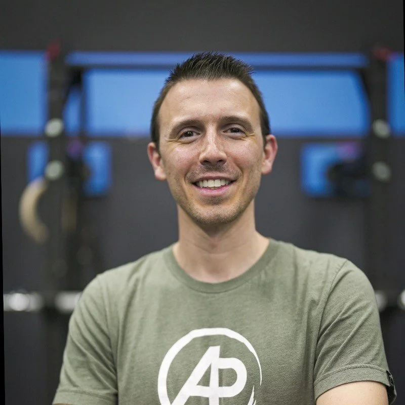 Smiling person wearing a green T-shirt with AP logo in a gym setting.