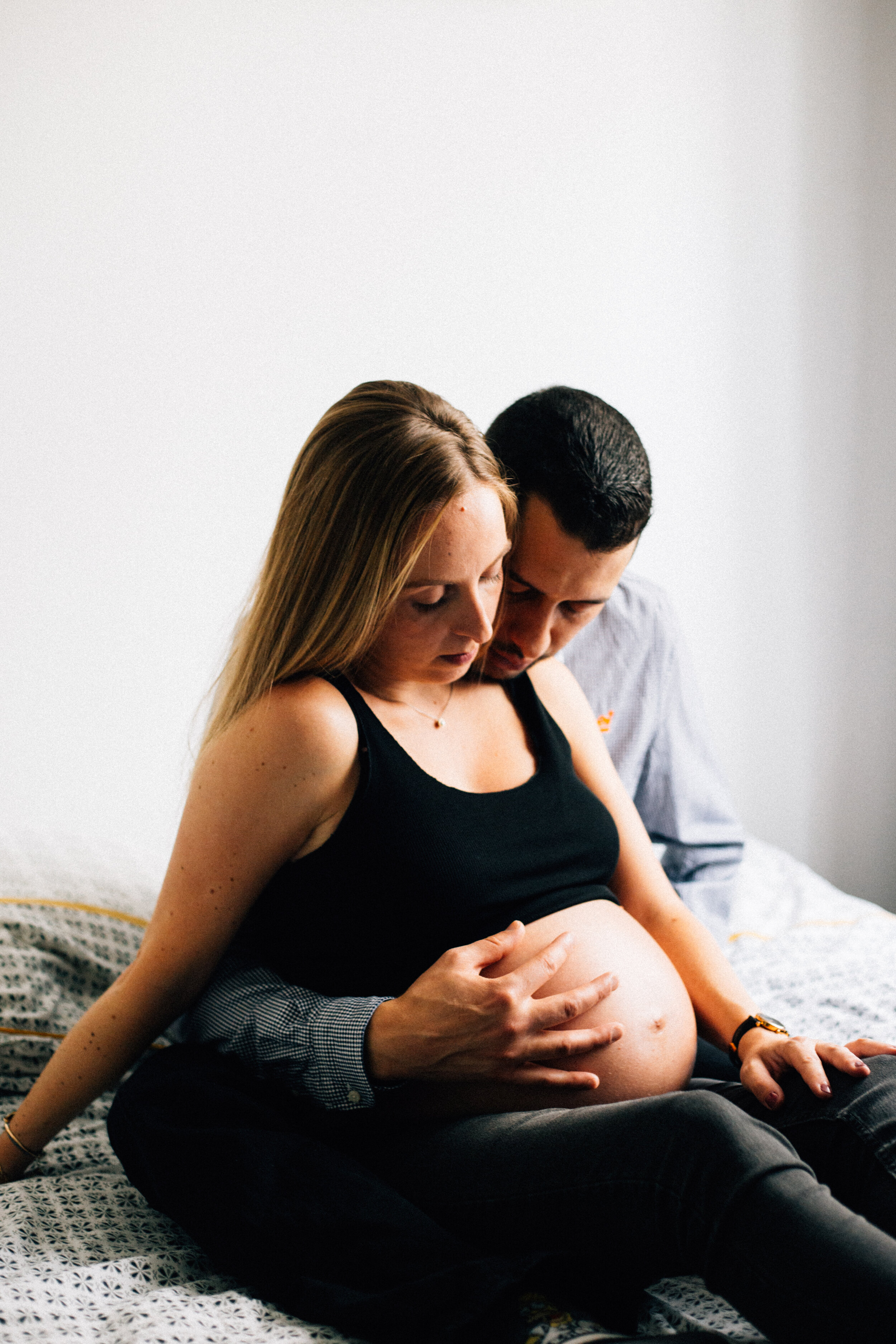 séance photo couple grossesse assis sur leur lit à domicile