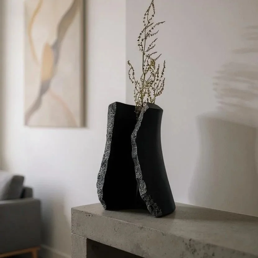 Vase en granite noir avec des détails texturés, posé sur une console en marbre dans un salon moderne.