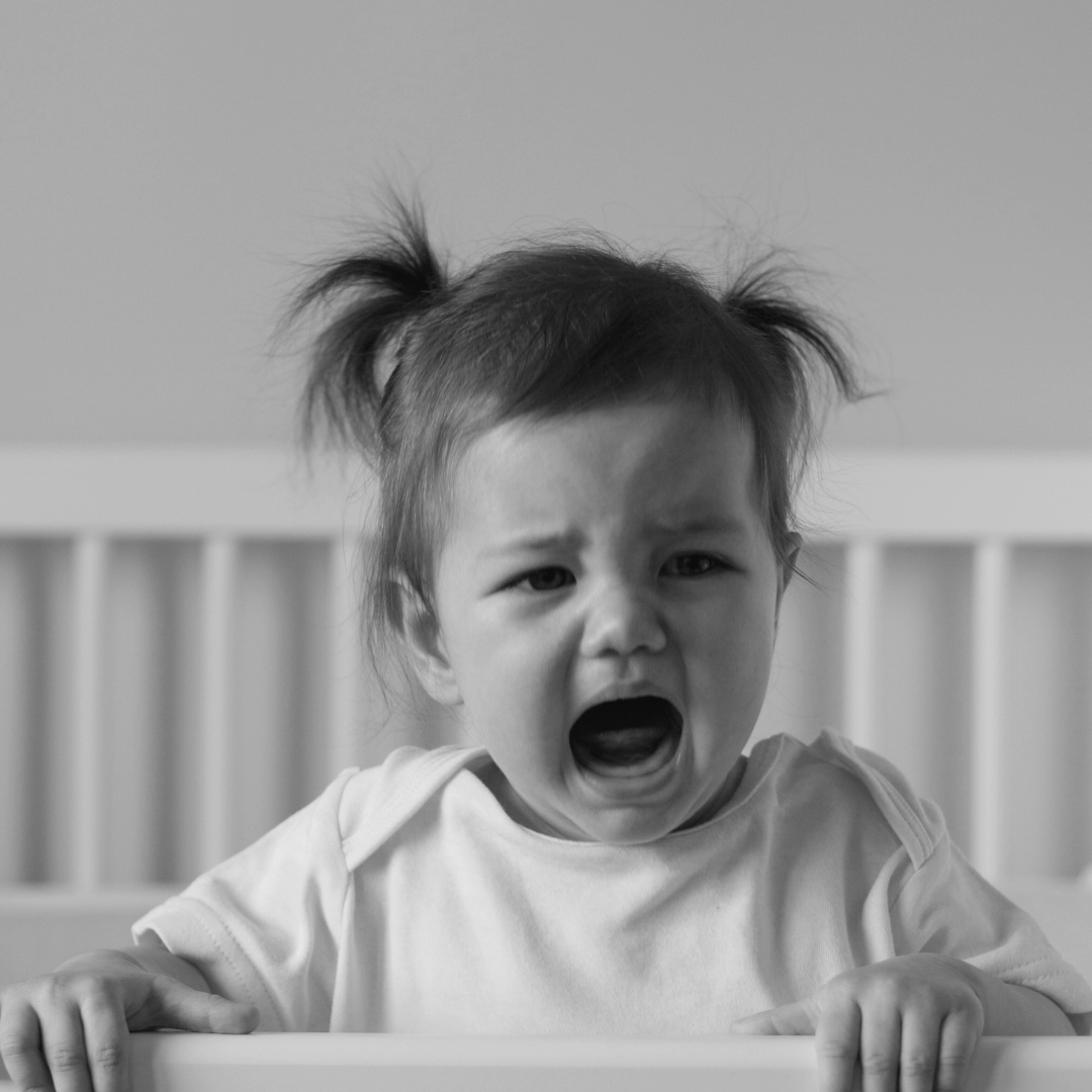 A young child with pigtails crying in a crib.