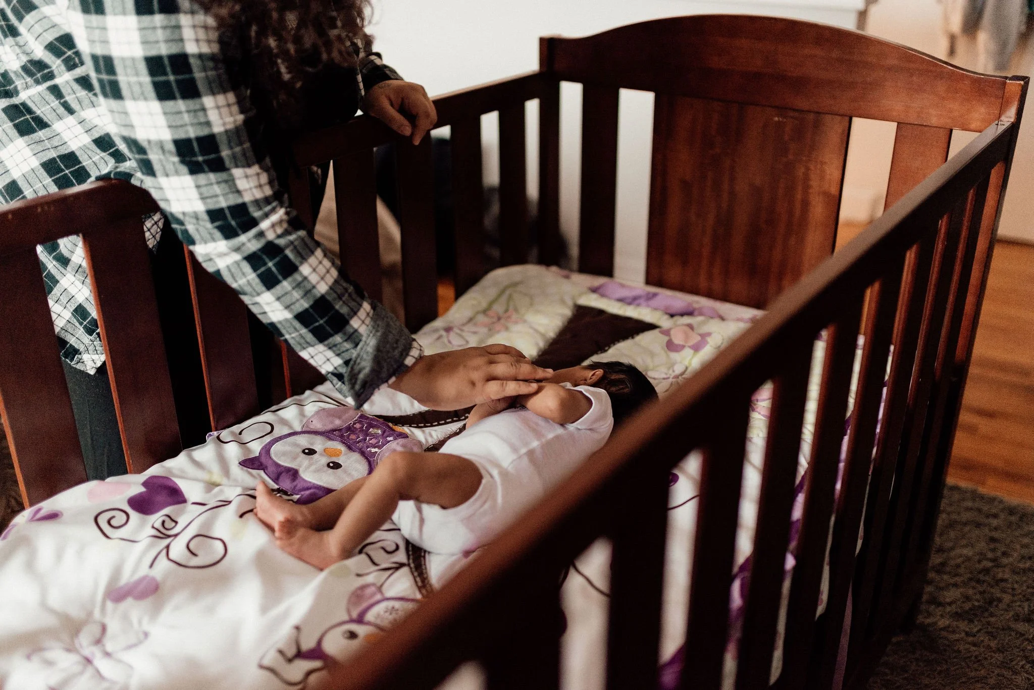 Newborn sleeping in the crib with parent touching their arm