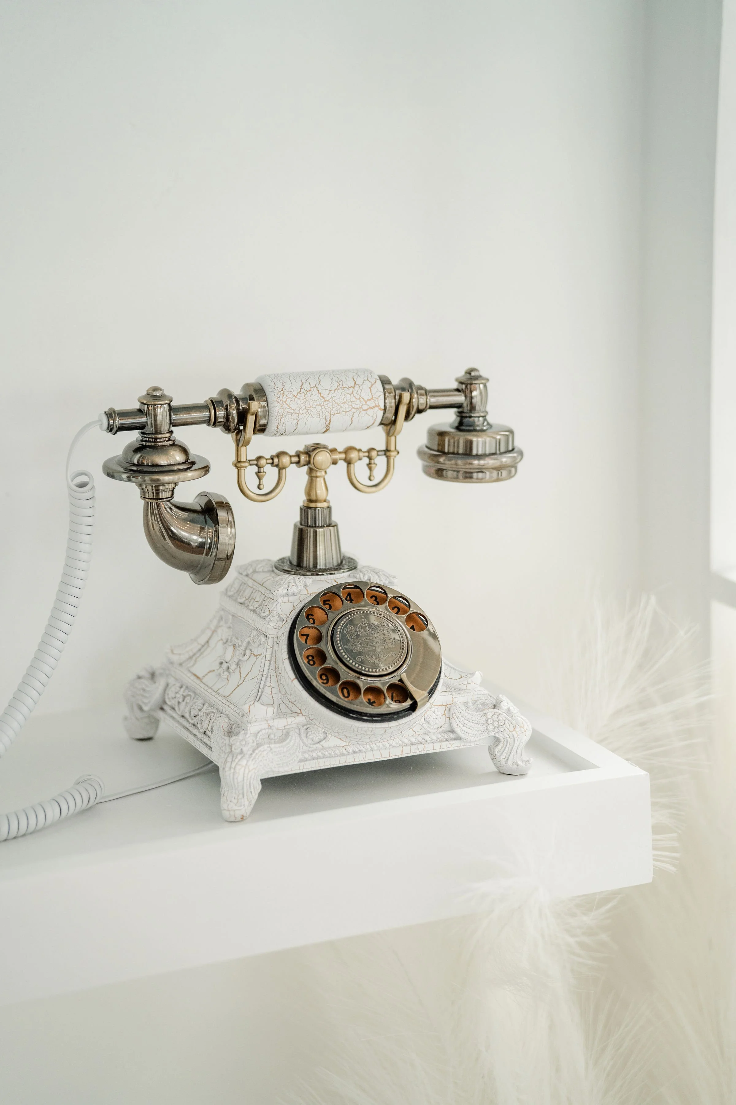 Vintage rotary telephone with ornate white and gold design on a white surface against a light background.