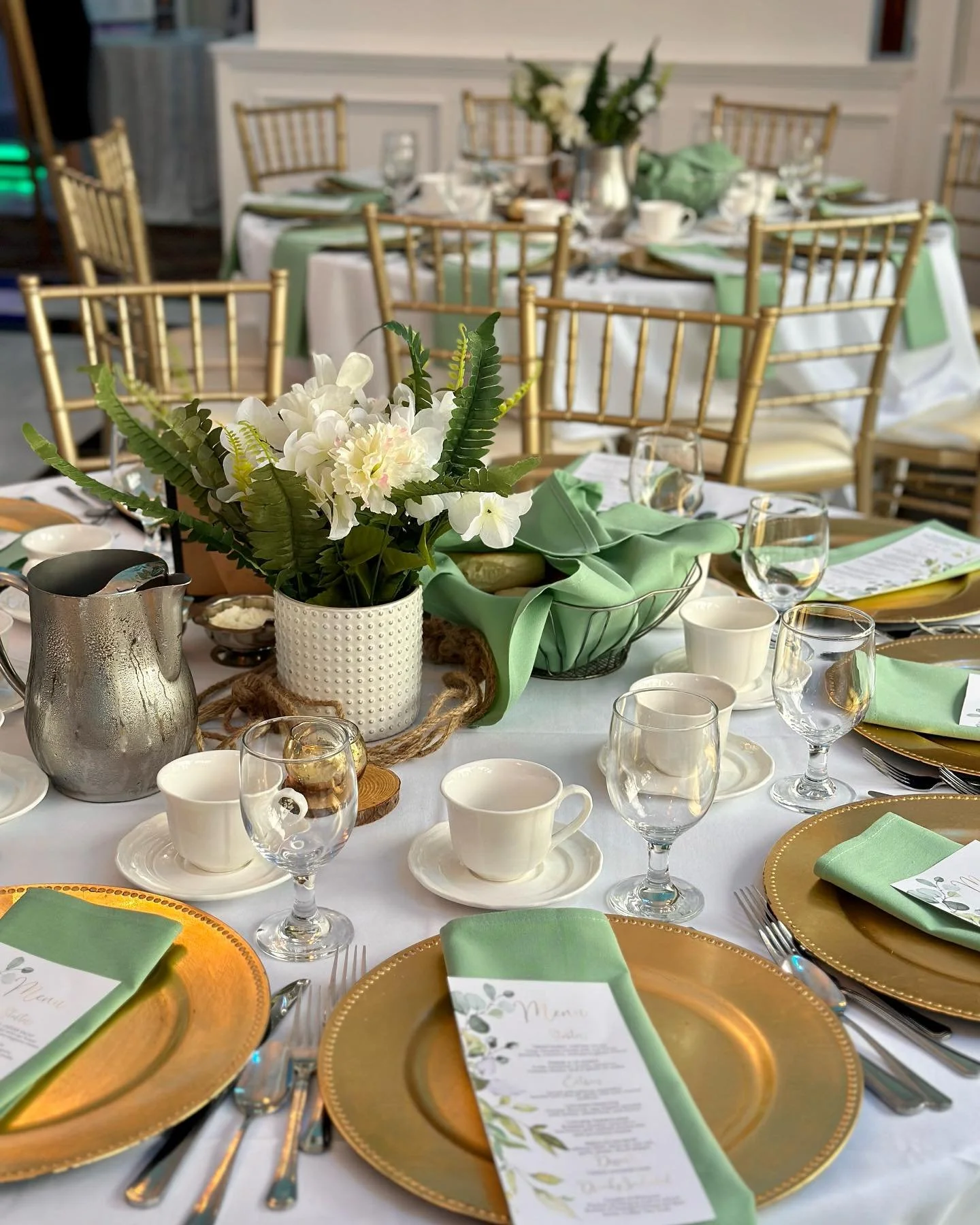 A beautifully set dining table with gold chargers, green napkins, and a floral centerpiece.