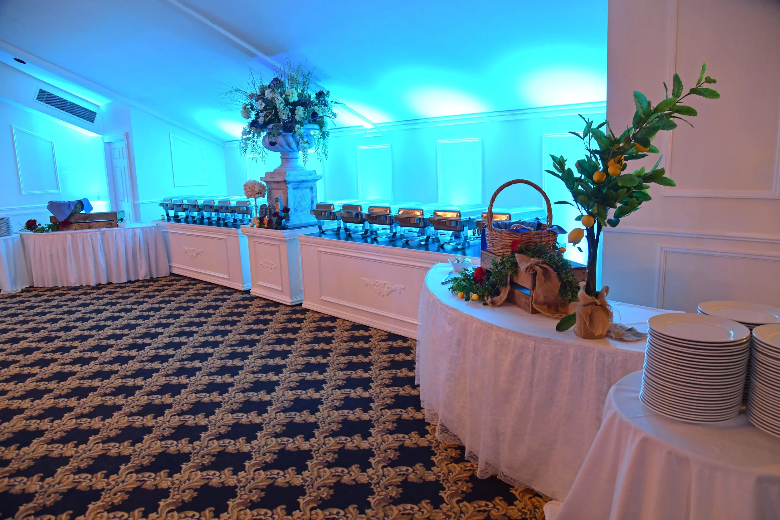 Wedding reception setup with a buffet table, floral arrangements, and blue ambient lighting in an elegant room.
