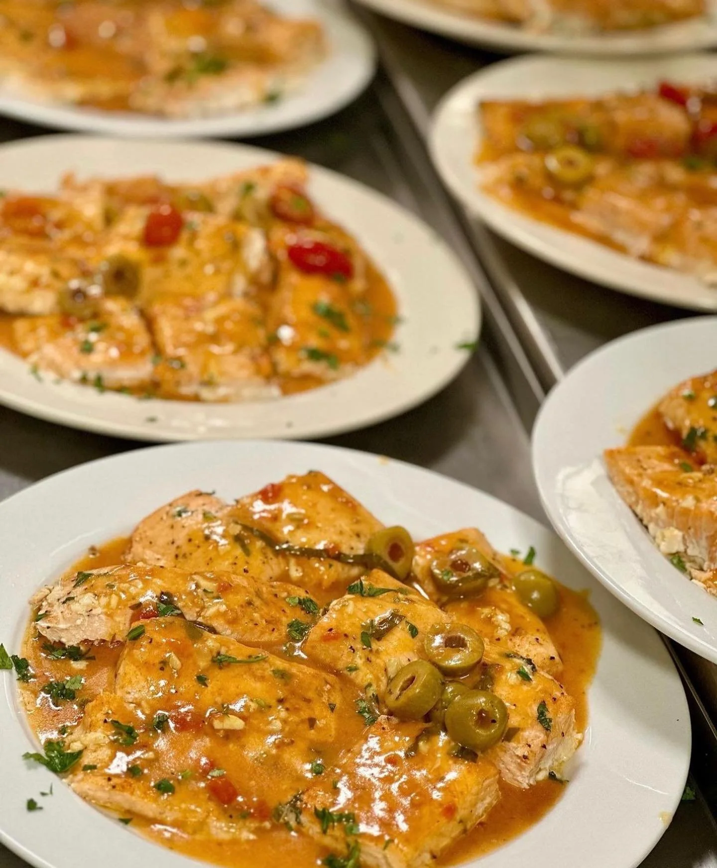 Plates of chicken with orange sauce and green olives garnished with chopped herbs.