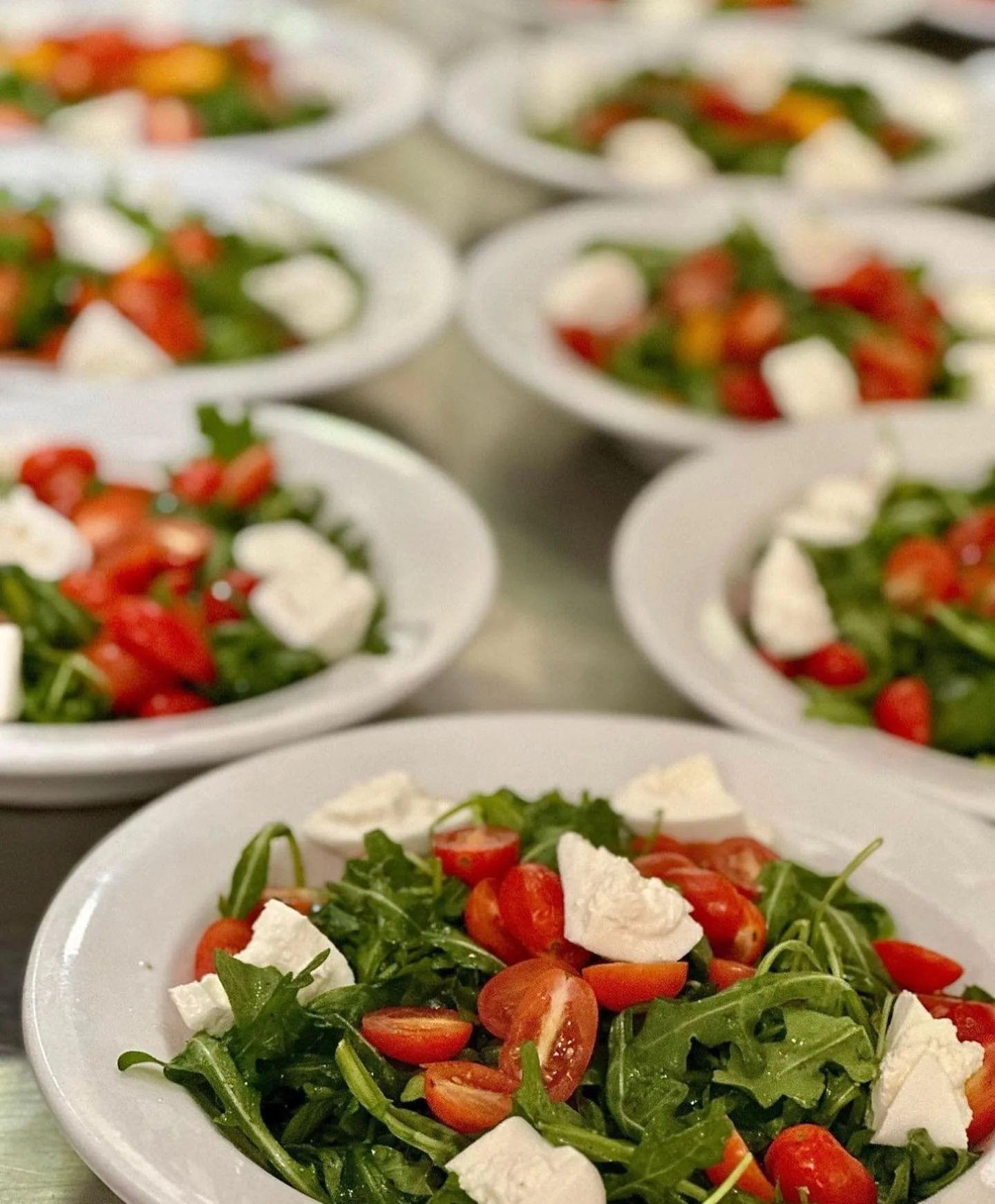 Salad with cherry tomatoes, arugula, and mozzarella cheese on white plates.