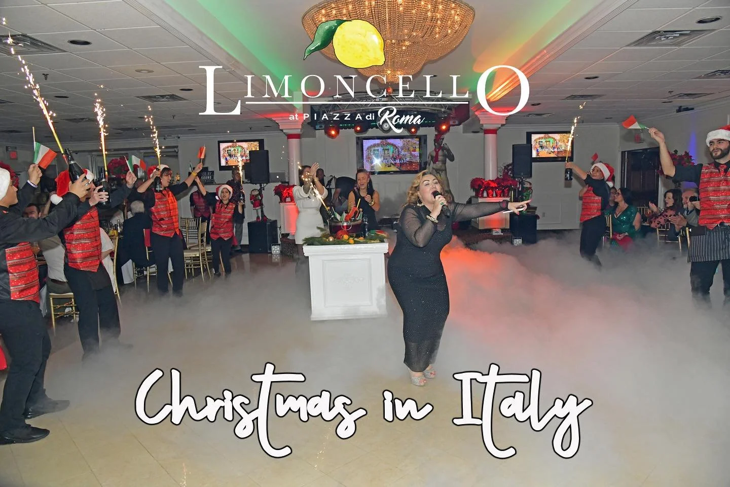 A woman singing into a microphone at a Christmas celebration in Italy, with dancers holding small Italian flags and sparklers, in an elegantly decorated banquet hall with Christmas decorations.