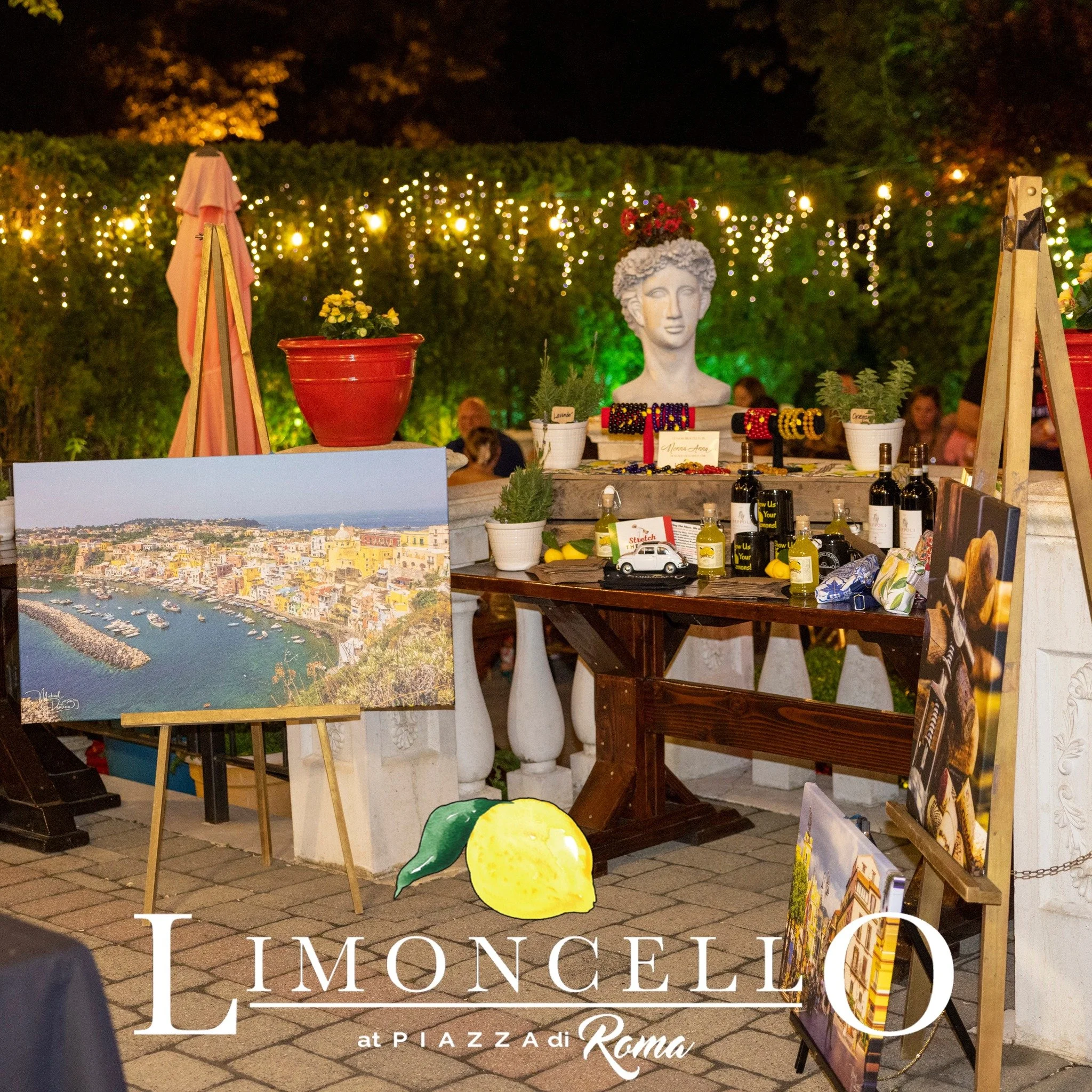 Outdoor night scene at Piazza di Roma, Rome, with art, jewelry, and souvenir displays illuminated by string lights, greenery, and a decorative bust statue.