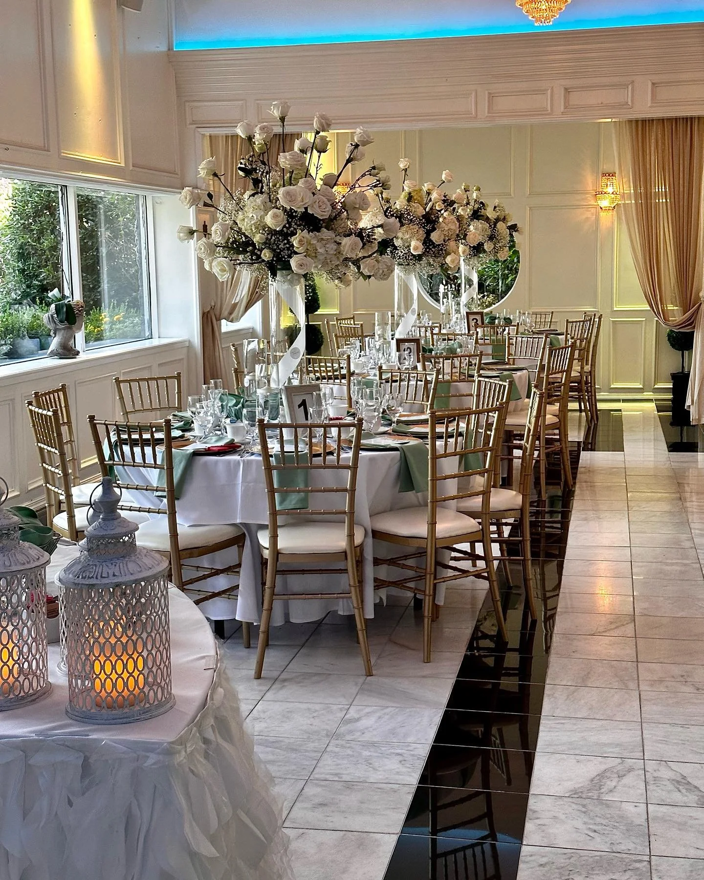Decorated banquet hall with round tables, gold chairs, white tablecloths, floral centerpieces, and lit candles.