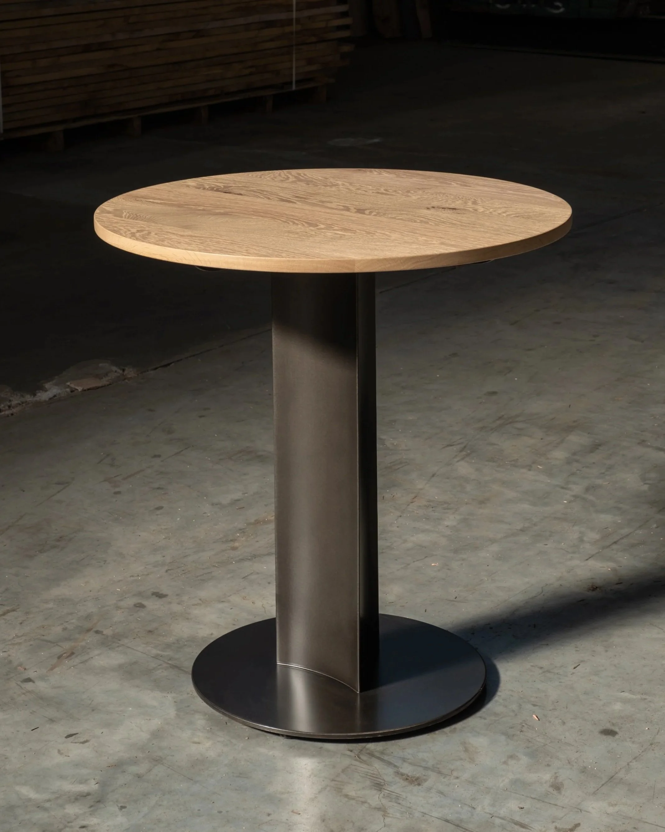 APEX bistro table in brushed metal and solid oak on concrete floor with hard shadow by frederik delbart