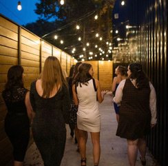 Group of women walking down an outdoor path with string lights overhead.