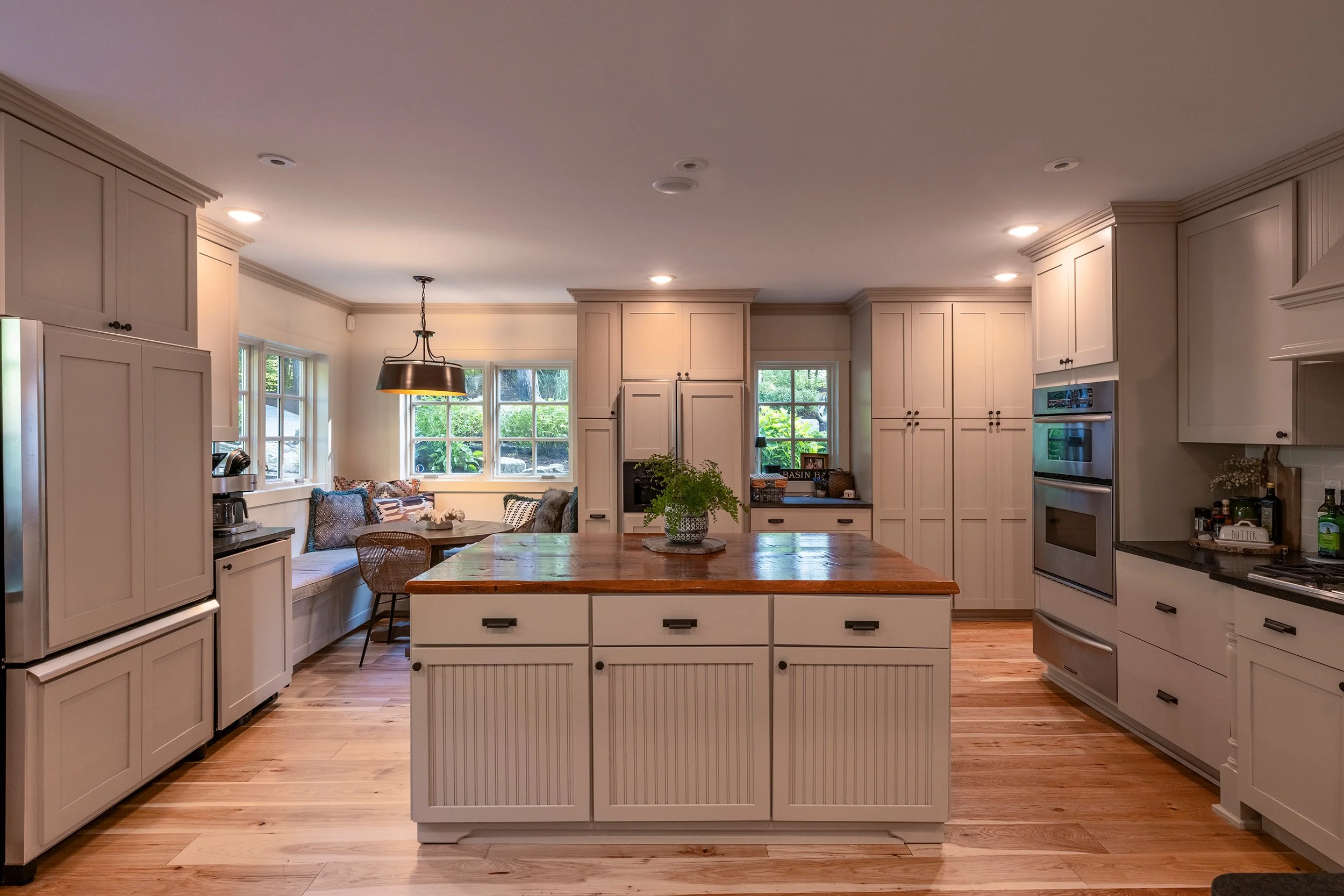 Kitchen with white cabinetry, wooden island, hardwood floors, and a dining nook with built-in bench and cushions near windows.