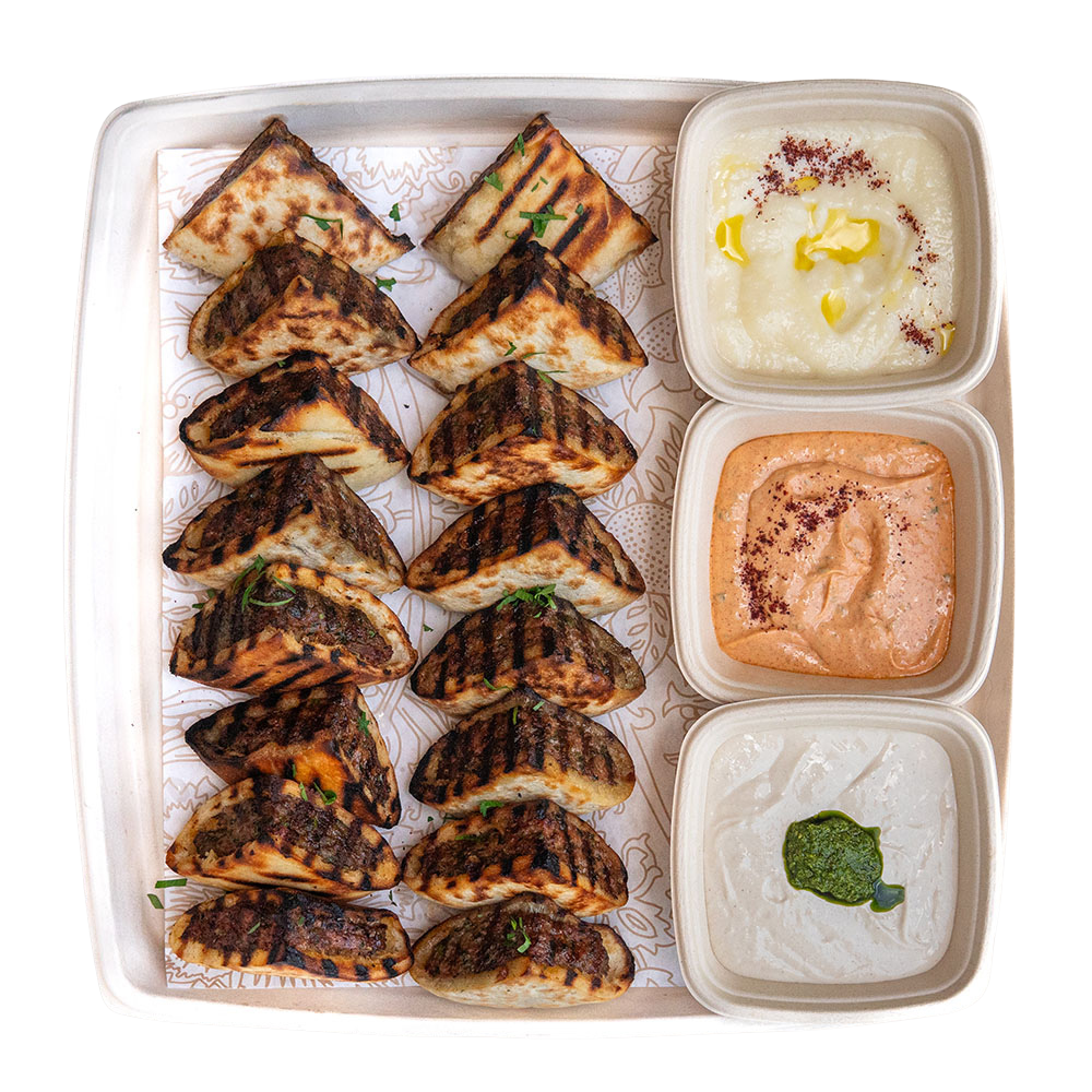 A tray with grilled paneer tikka arranged in rows on the left and three bowls of different types of sauces or dips on the right
