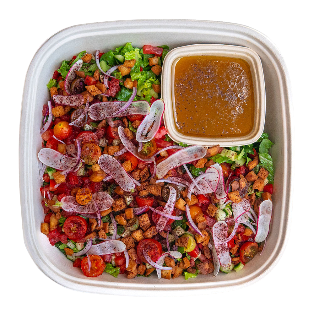 Fresh salad with cherry tomatoes, sliced red onions, chopped lettuce, and croutons in a takeout container with a side of dressing.