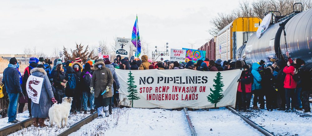  The crowd holds a protest banner at a Wet'suwet'en Solidarity Event at the Rail Yard in Vaughan, Toronto, on Feb. 15, 2020.  (Jason Hargrove/Flickr via Global Citizen, https://www.globalcitizen.org/en/content/indigenous-people-in-canada-protesting-p