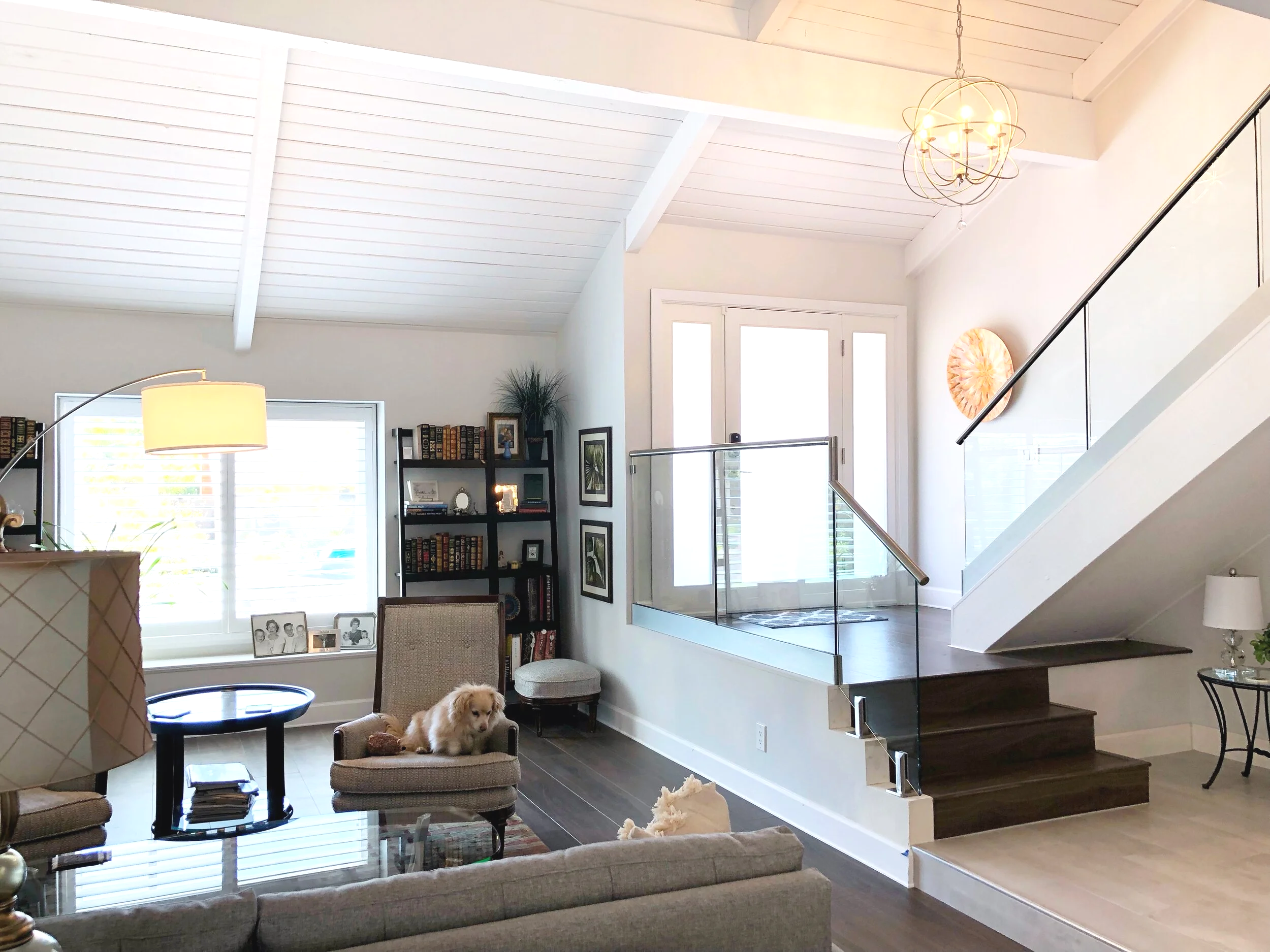 California casual living room with a vaulted plank ceiling, exposed beams, an orb chandelier, and a glass-railing staircase by Gin Treadwell Interiors in Santa Clarita.