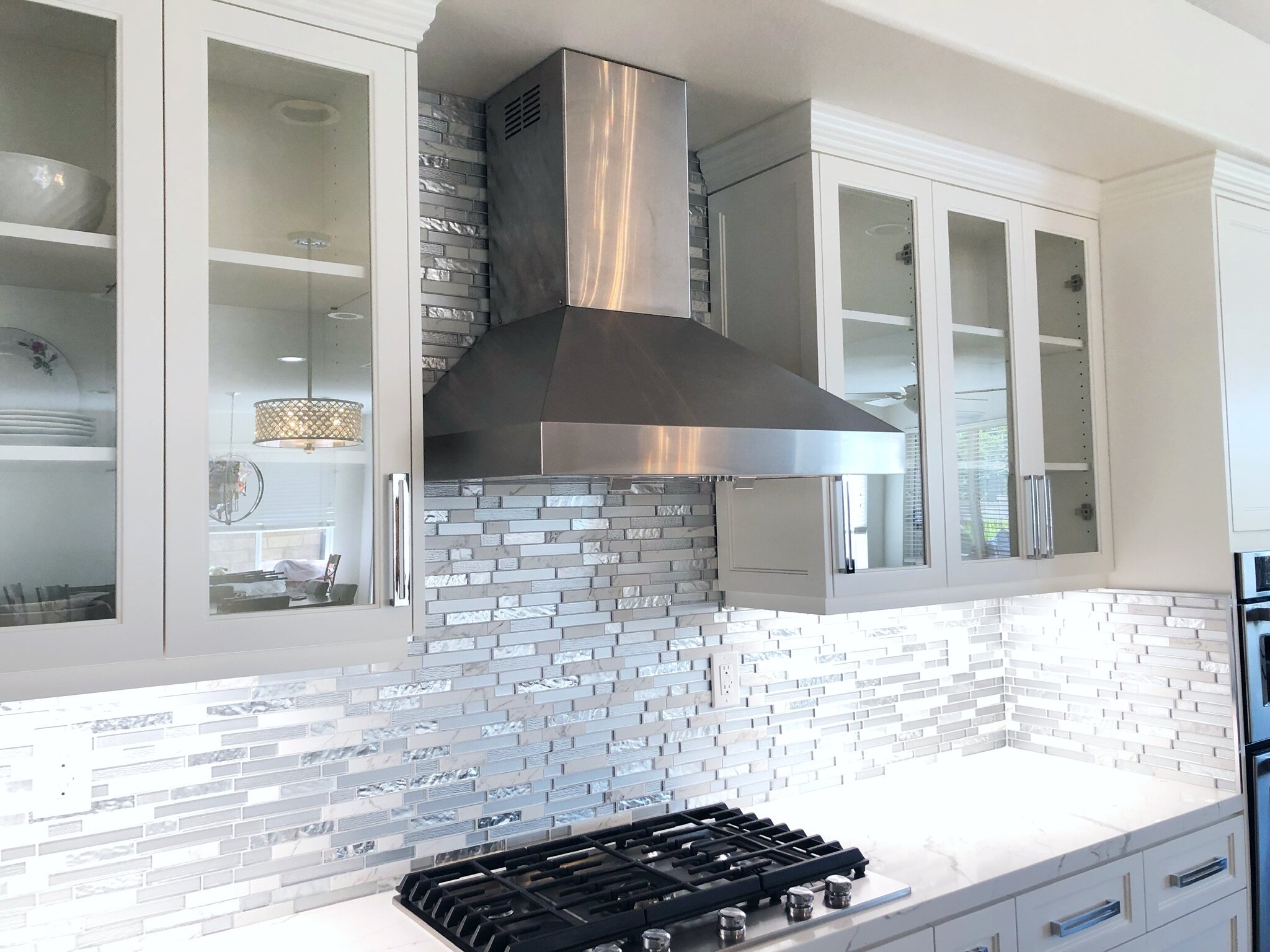 Modern farmhouse kitchen with a stainless range hood, glass tile backsplash, and marble countertops by Gin Treadwell Interiors in Los Angeles.
