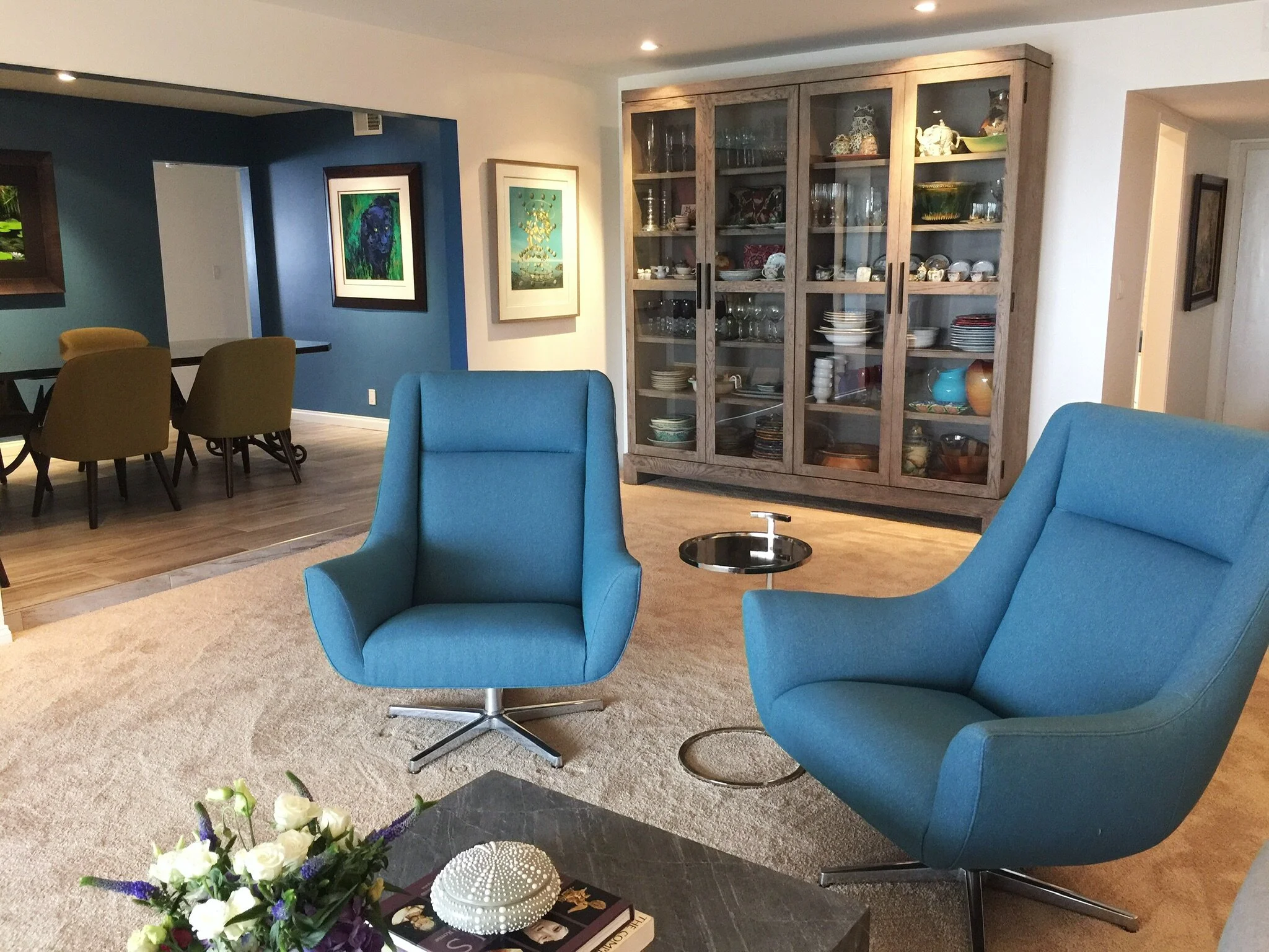 Modern eclectic living room with blue accent chairs and a glass display cabinet by Gin Treadwell Interiors in Santa Clarita.