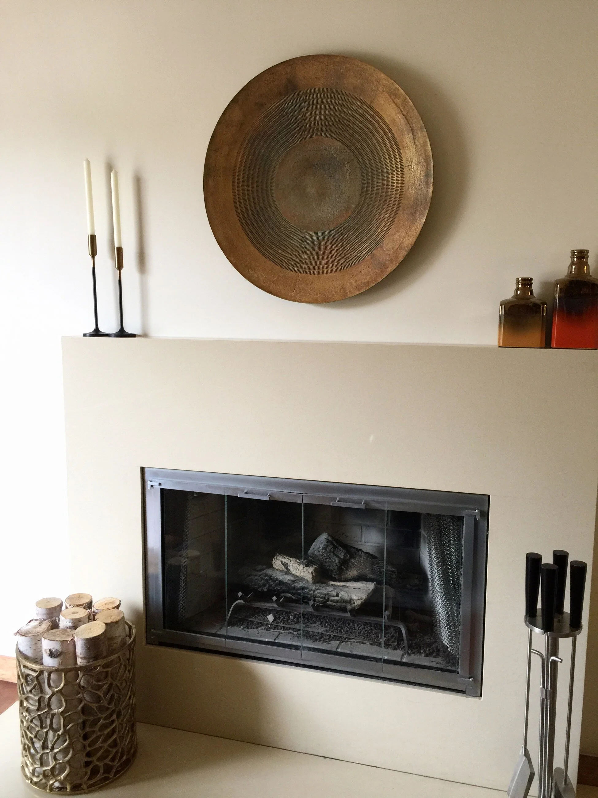 Spanish style fireplace with a plaster surround, a woven wall basket, and layered candlesticks on the mantel by Gin Treadwell Interiors in Santa Clarita.