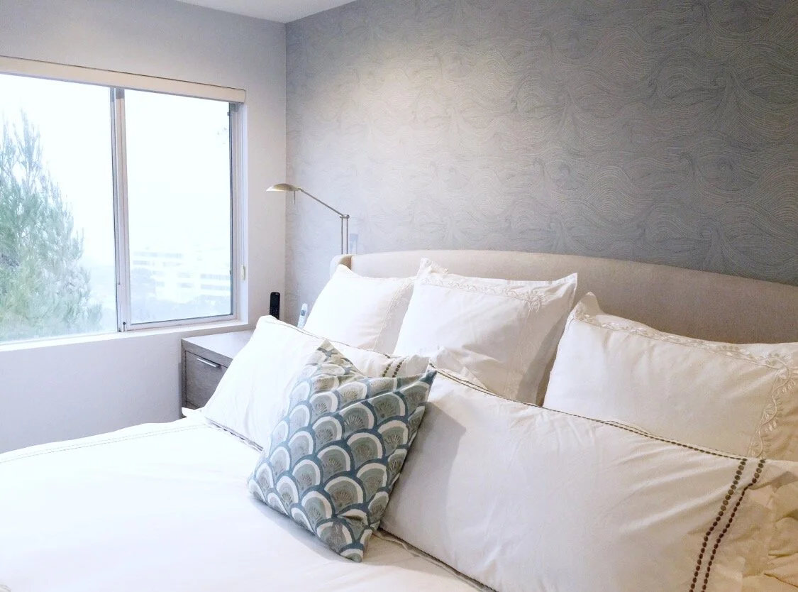 Modern eclectic bedroom with layered white bedding and textured gray walls by Gin Treadwell Interiors in Santa Clarita.