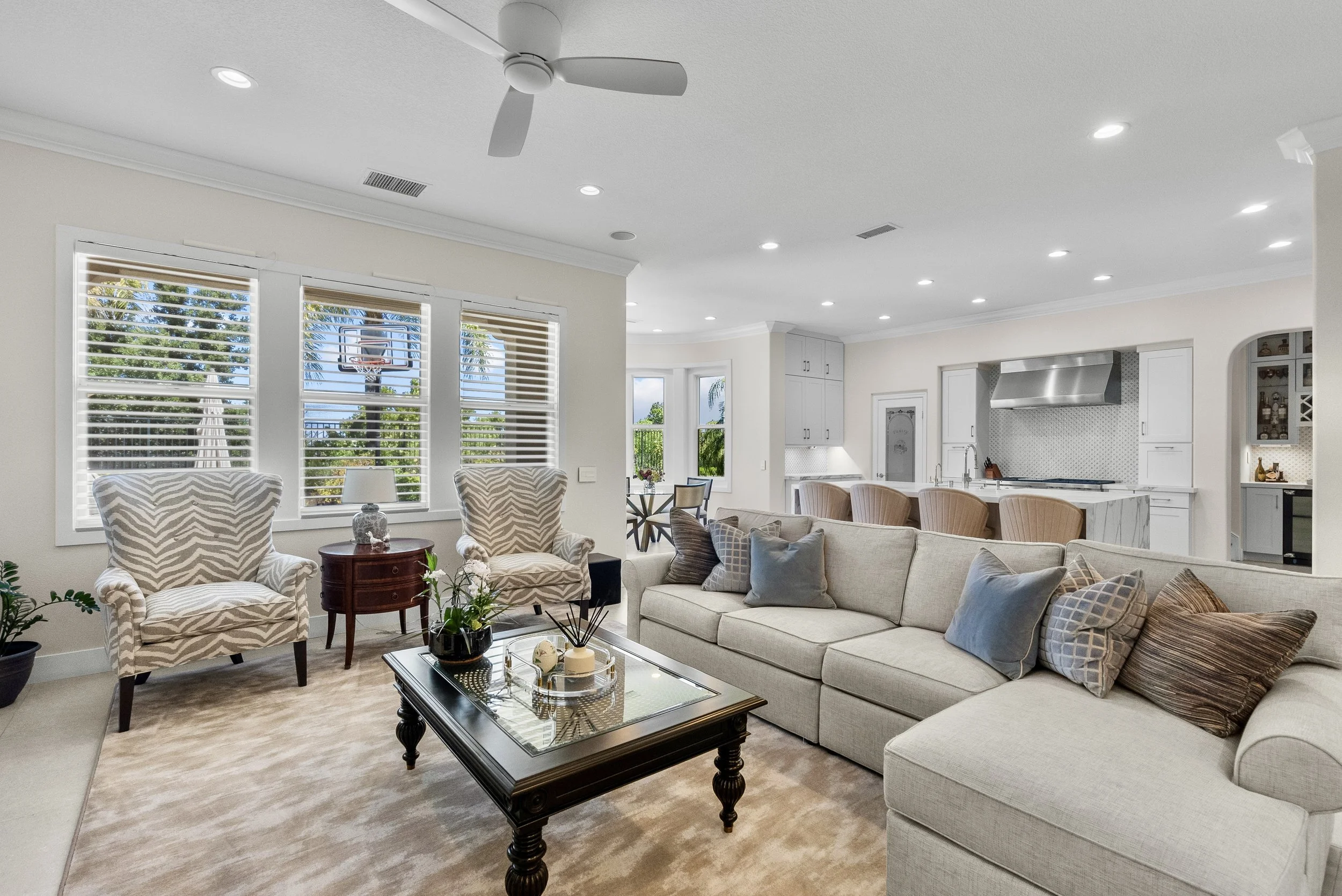 Traditional living room with a neutral sectional, classic coffee table, and large shuttered windows by Gin Treadwell Interiors in Santa Clarita.