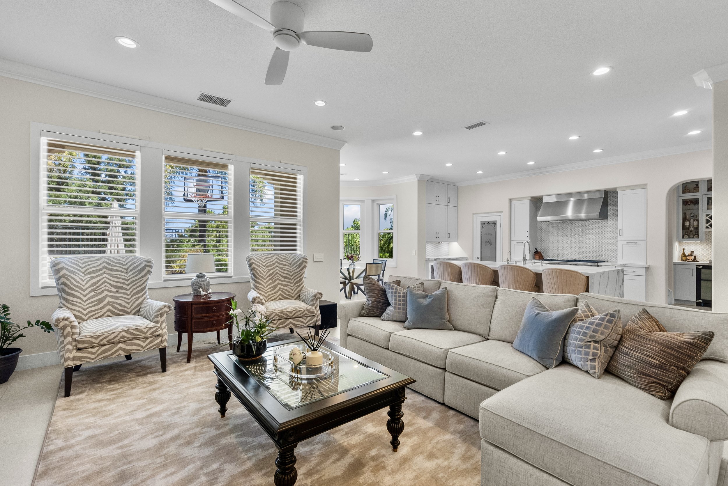 Traditional living room with a neutral sectional, classic coffee table, and large shuttered windows by Gin Treadwell Interiors in Santa Clarita.