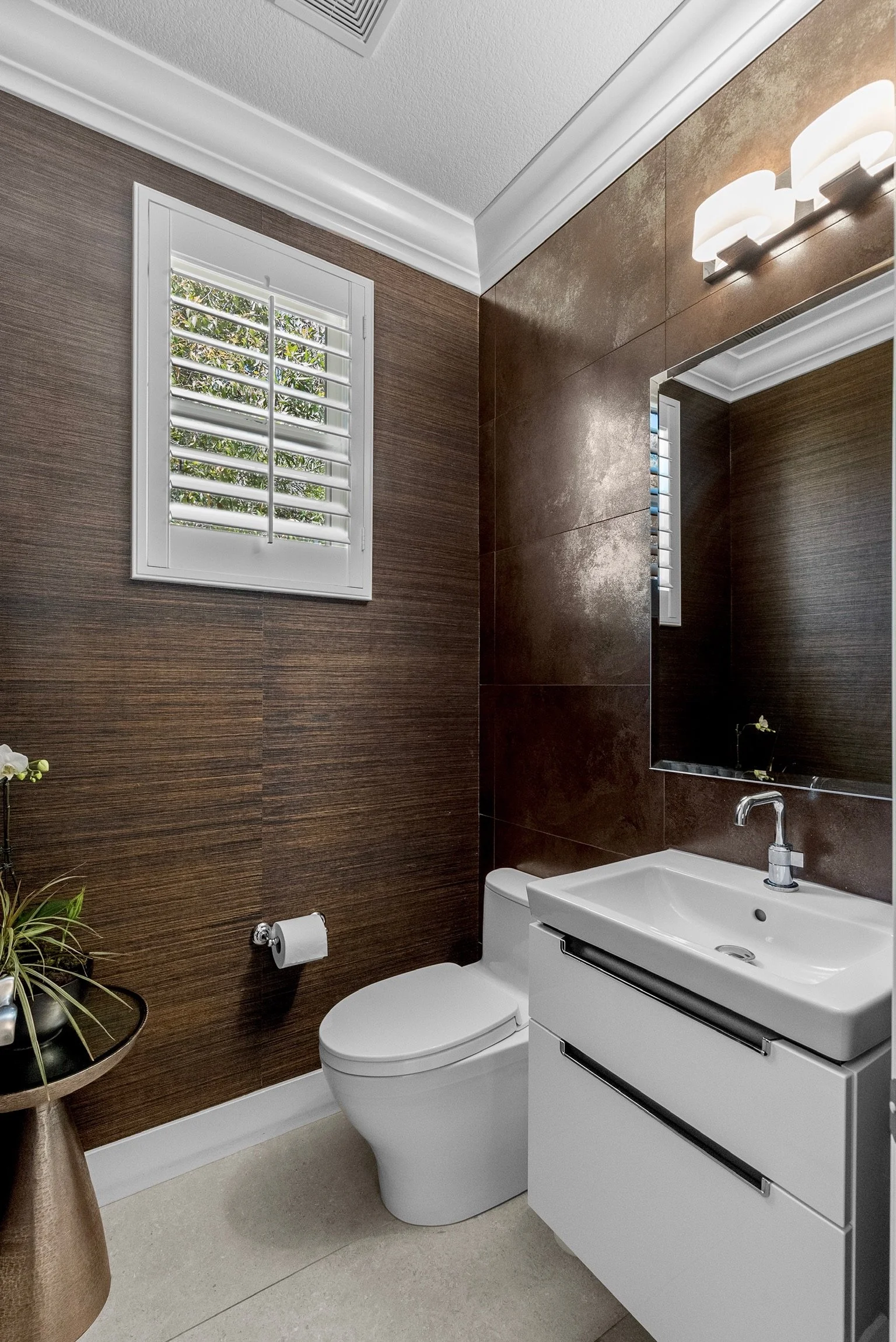 Residential interior design by Gin Treadwell Interiors, a powder room with dark grasscloth walls, a bronze tile accent wall, and a white floating vanity in Santa Clarita.