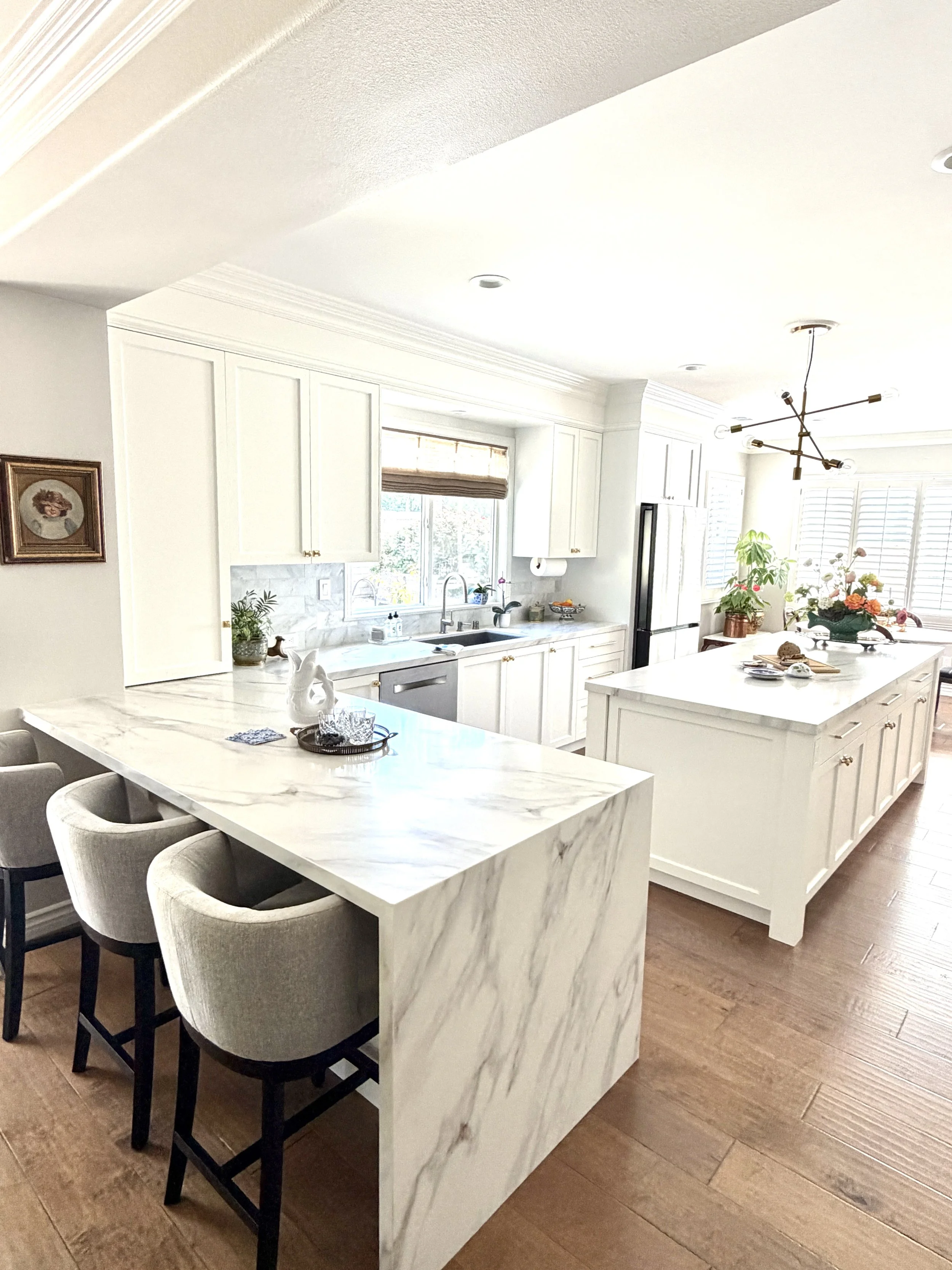 Traditional kitchen with white cabinetry, a marble island, and upholstered counter stools by Gin Treadwell Interiors in Santa Clarita.