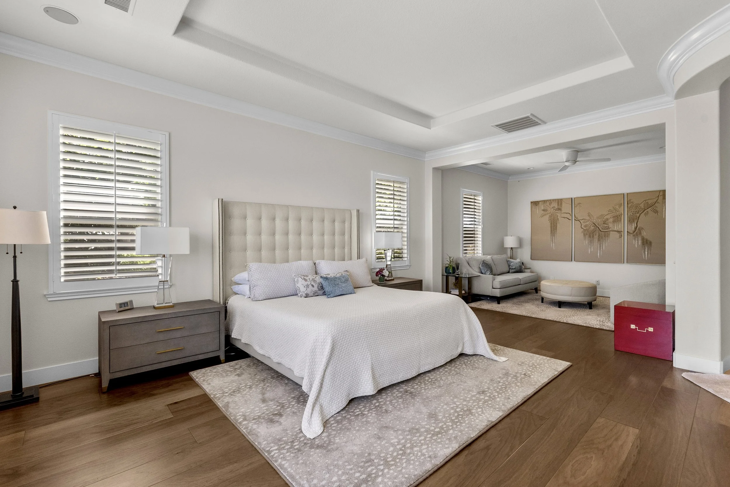 Traditional primary bedroom with an upholstered headboard, neutral bedding, and a tray ceiling by Gin Treadwell Interiors in Santa Clarita.