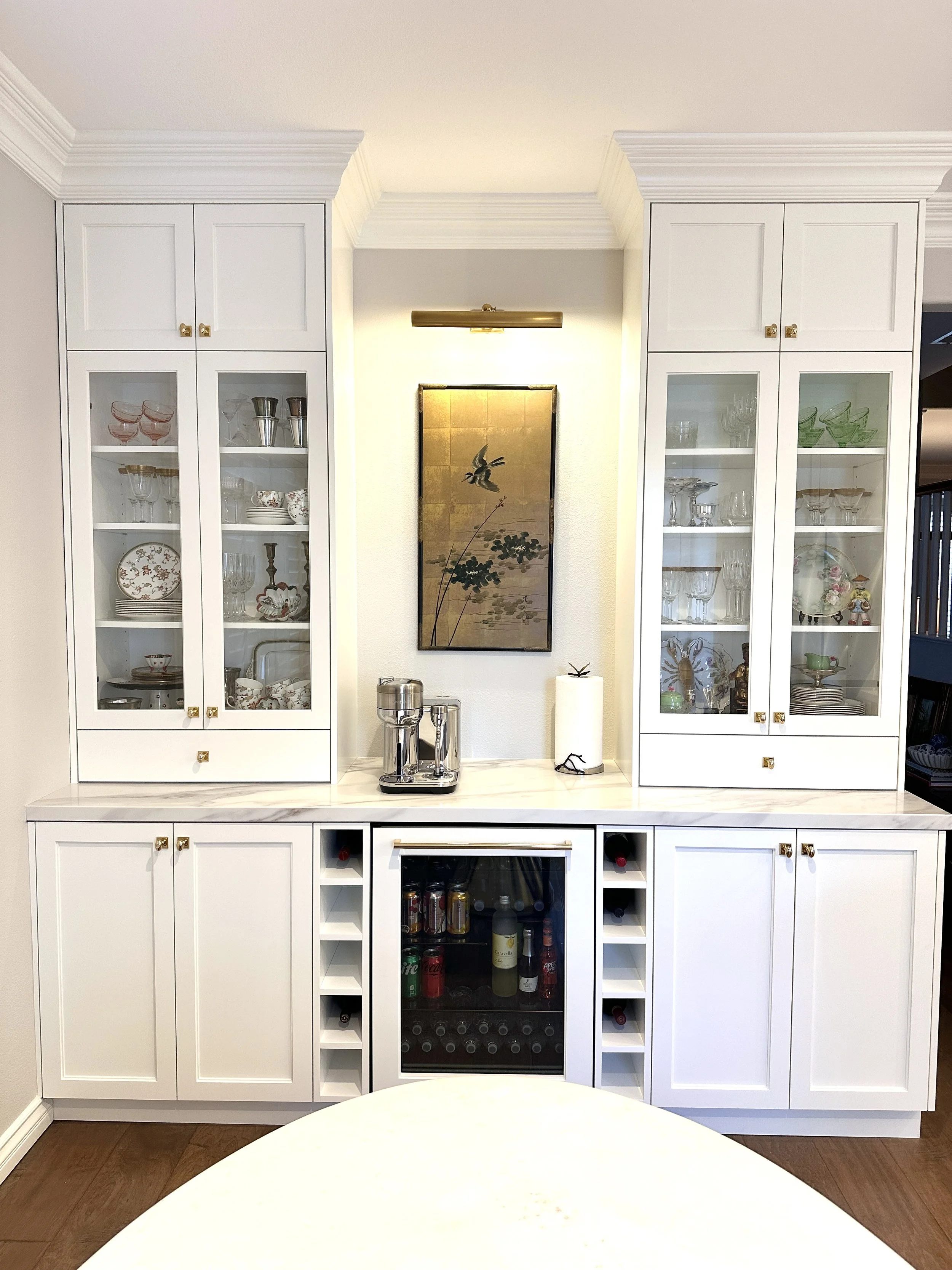 Traditional built-in cabinetry with glass-front cabinets, framed art, and wine storage by Gin Treadwell Interiors in Santa Clarita.