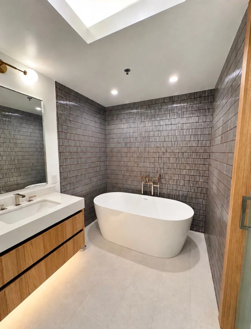 Organic modern bathroom with a freestanding tub and dark tile wall by Gin Treadwell Interiors in Santa Clarita.