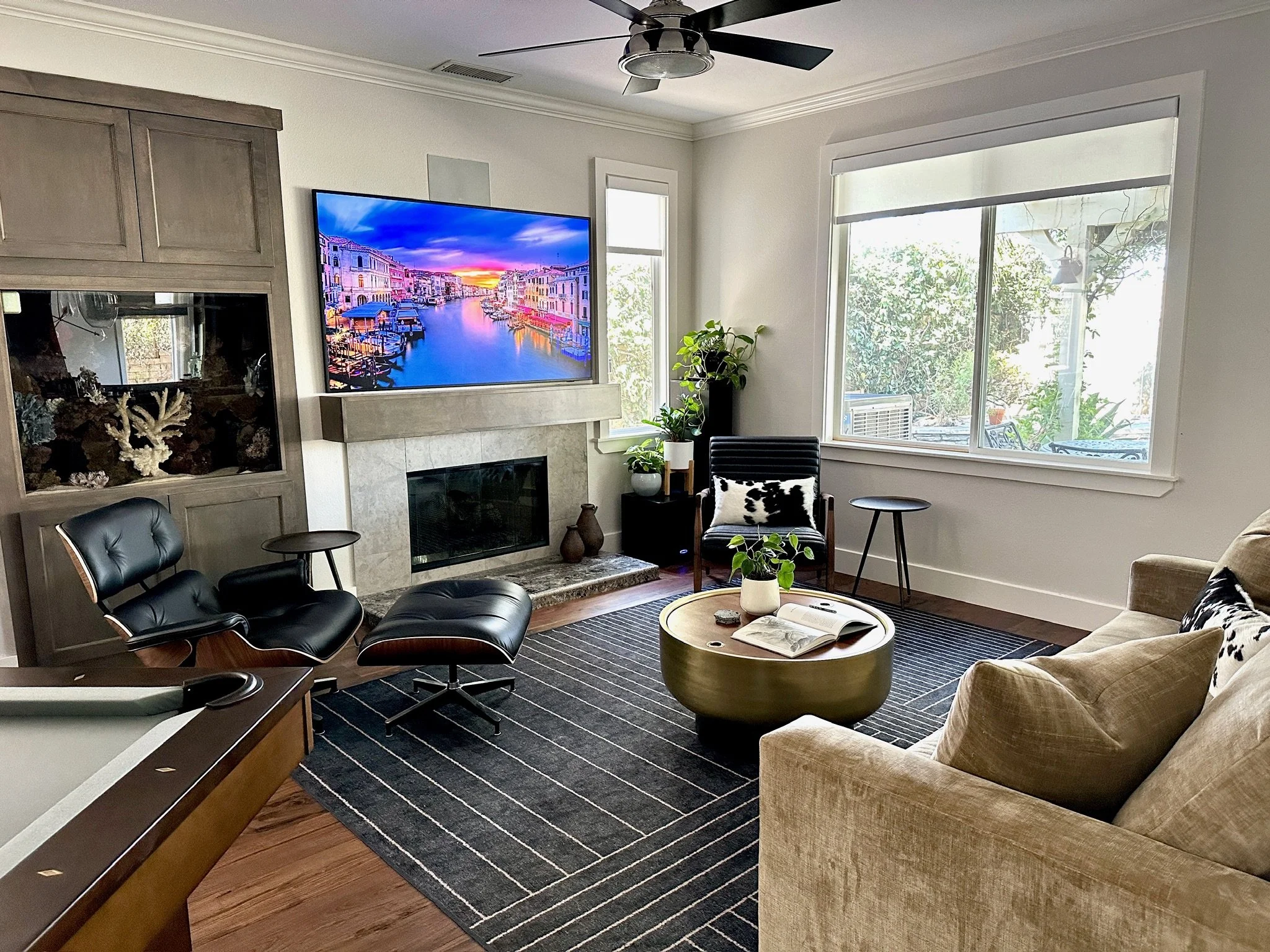 Residential interior design by Gin Treadwell Interiors, a family room with a black leather lounge chair, a fireplace with a mounted TV, and a built-in aquarium in Santa Clarita.