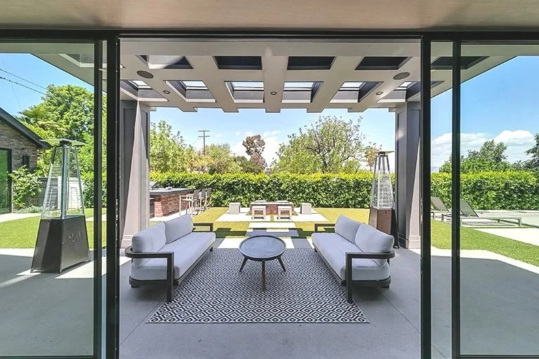 Organic modern covered patio with a wood pergola, lounge seating, and a patterned outdoor rug opening to the lawn by Gin Treadwell Interiors in Santa Clarita.