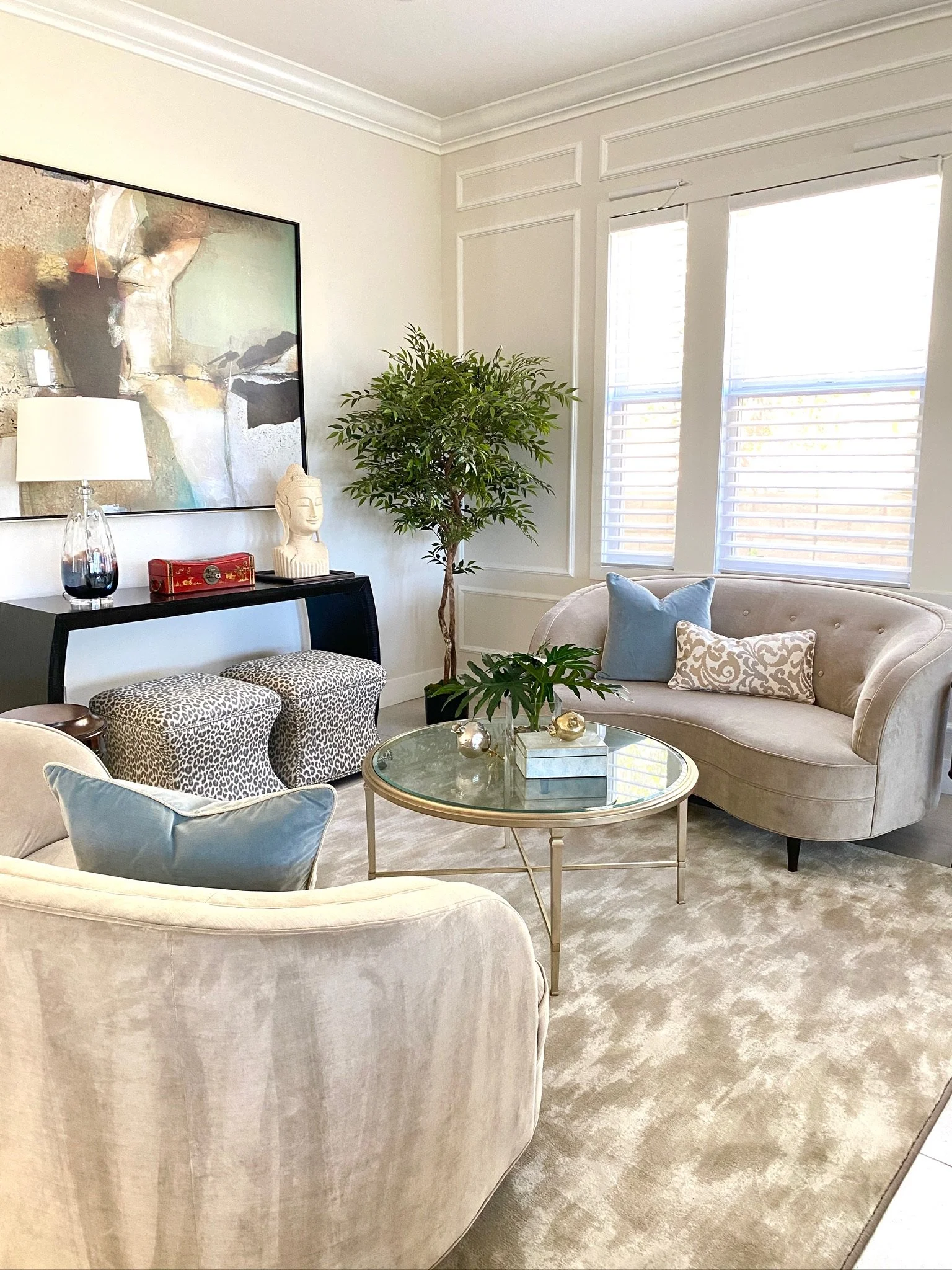 Residential interior design by Gin Treadwell Interiors, a formal living room with a curved velvet sofa, a glass coffee table, and abstract art in Santa Clarita.