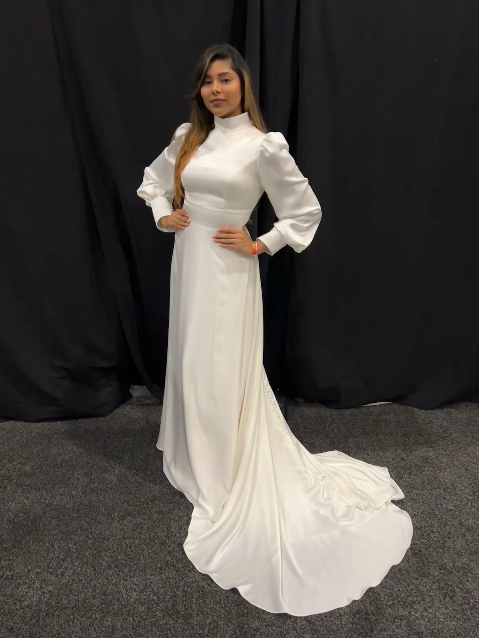 Woman in a white dress with long sleeves and a train, posed against a black backdrop.