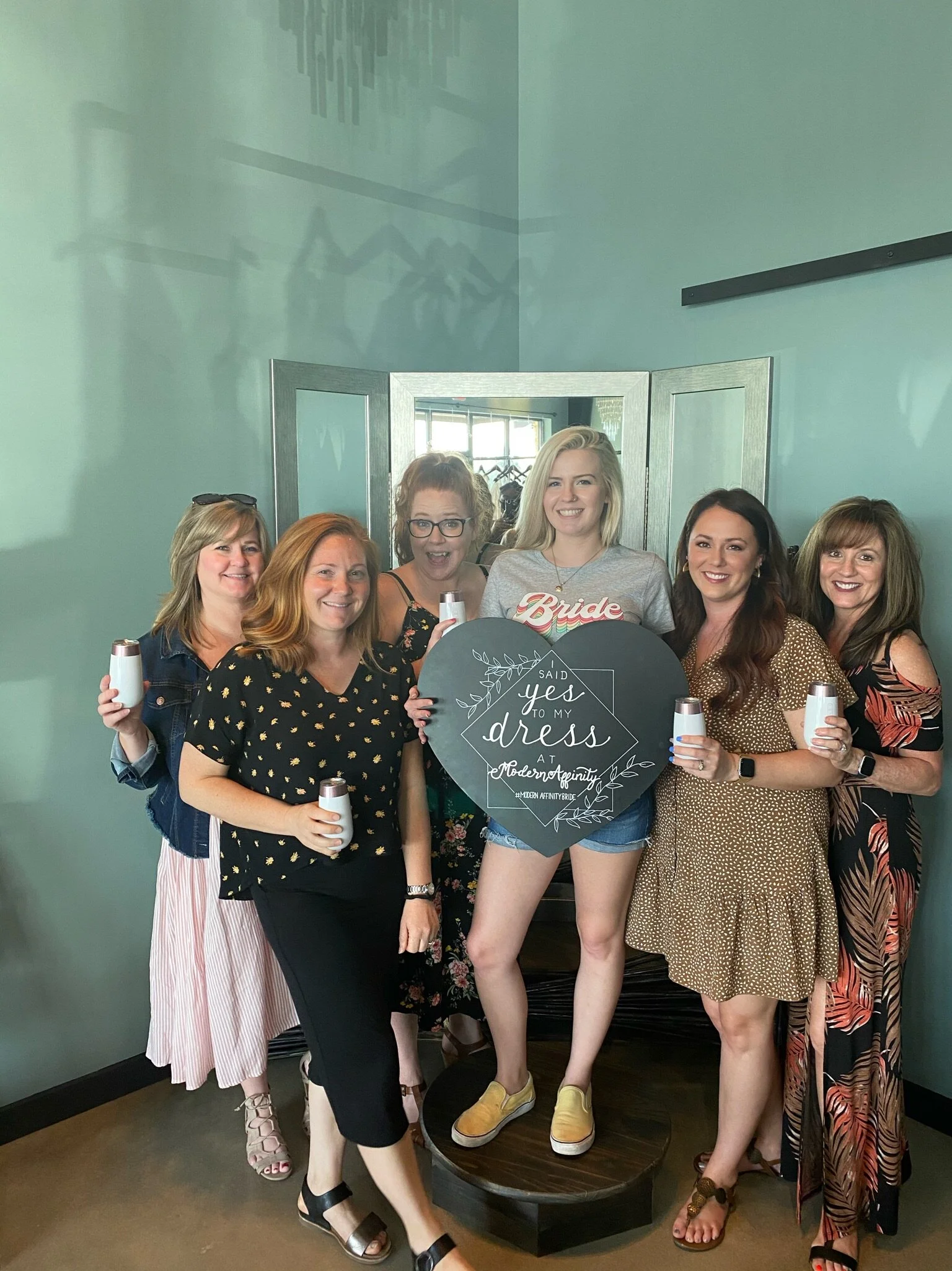 Group of women celebrating a bridal shower, holding candles, and standing behind a chalkboard sign that says, 'Said Yes to my dress at Modern Affinity, Modern Affinity Bride.'